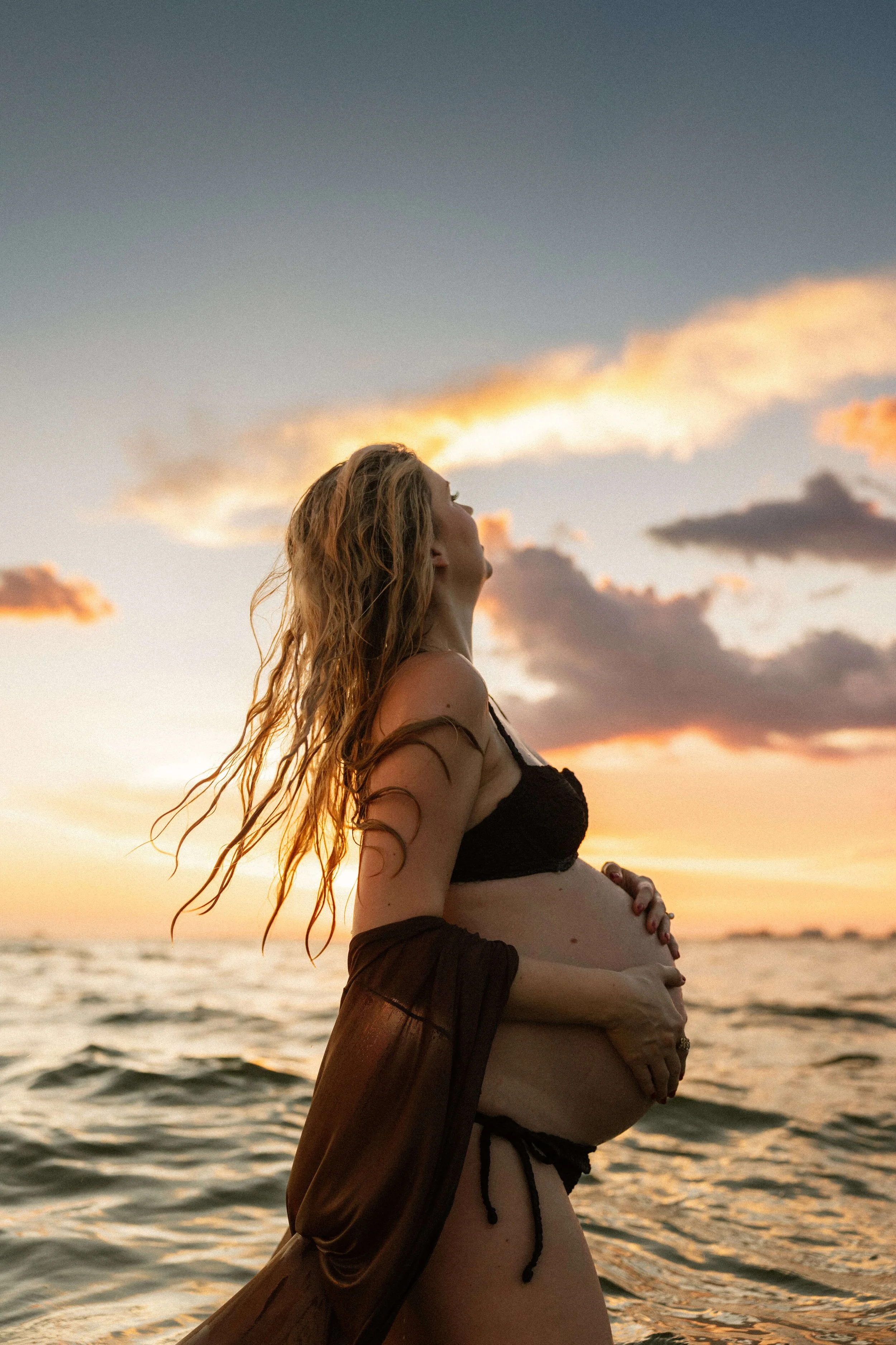 pregnant mom standing in the water in a bikini with her hair wet looking off into the distance on fort myers beach
