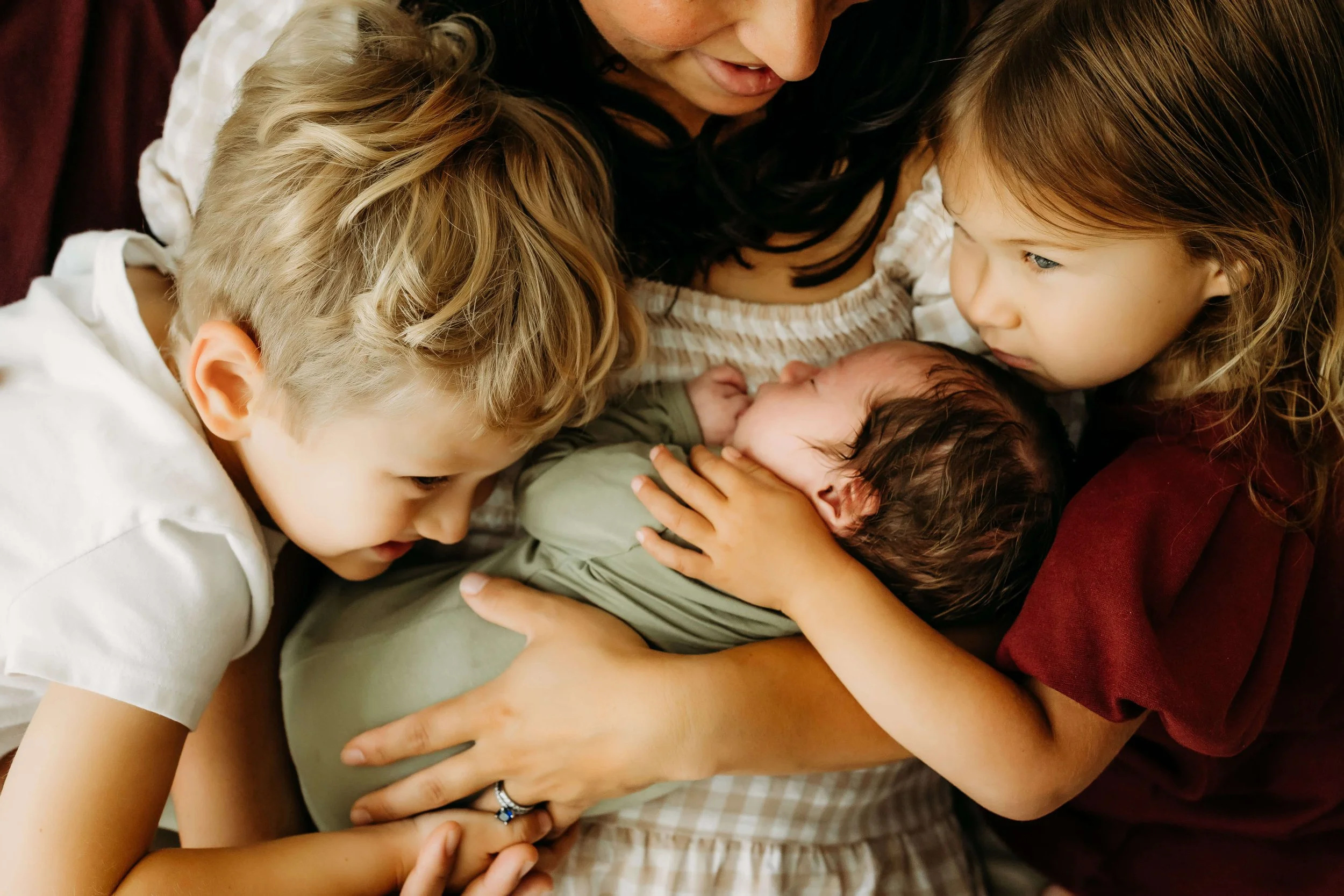 mama holding newborn baby boy while big brother and sister love on their new sibling