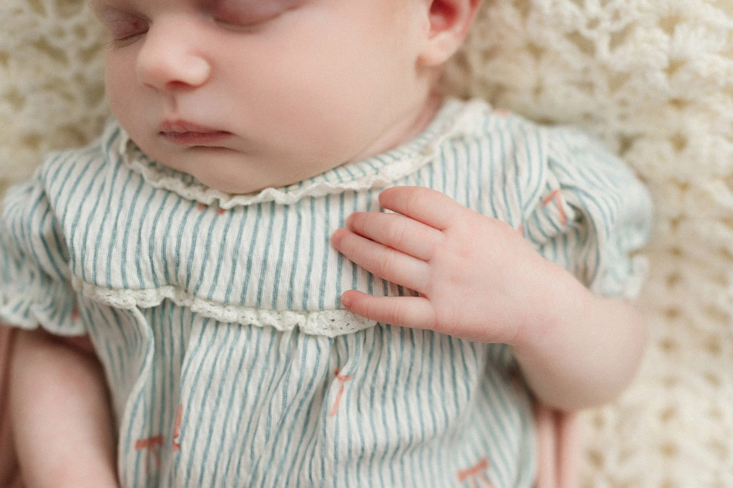 Close-up detail of a sleeping newborn baby's tiny hand resting on a blue striped outfit during a lifestyle newborn photography session in Fort Myers, Florida.