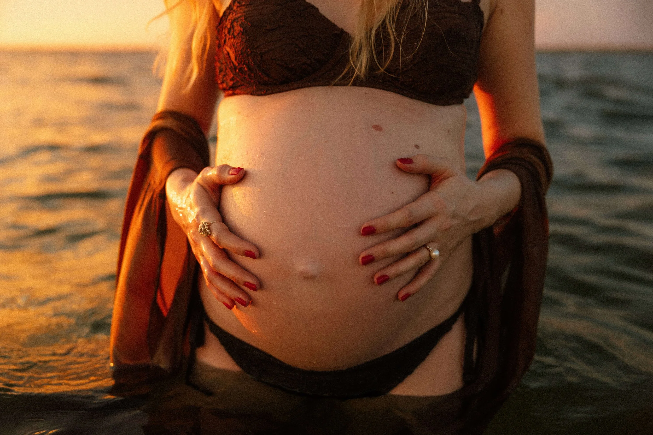pregnant woman in a bikini standing in the water holding her belly with her hands on Fort Myers Beach