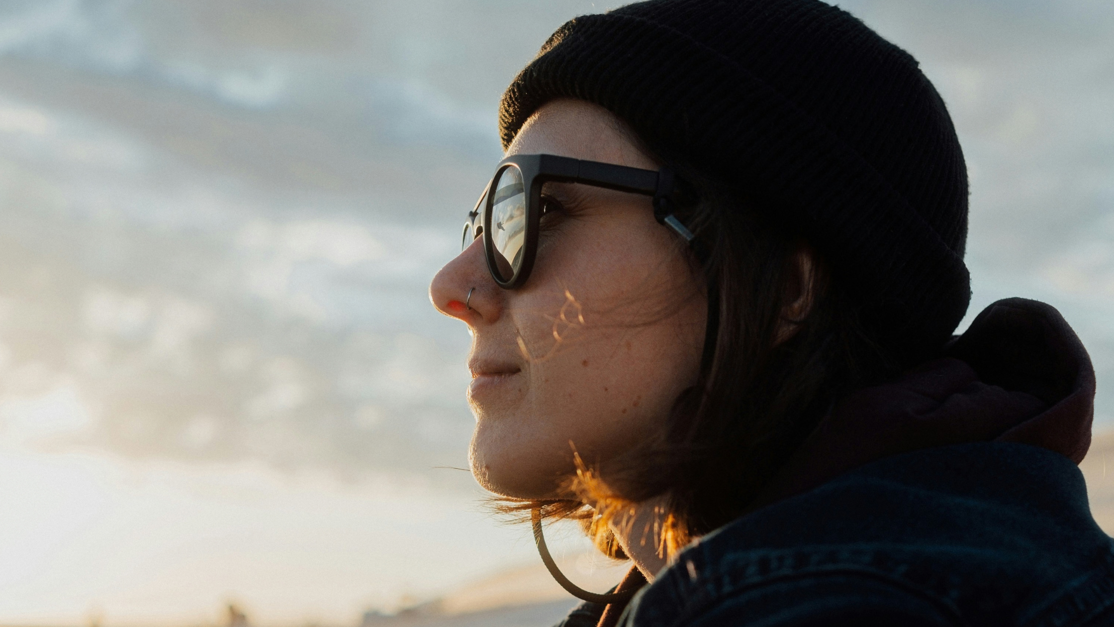 woman looking at the sunset, a paraglider in the reflection of her sun glasses
