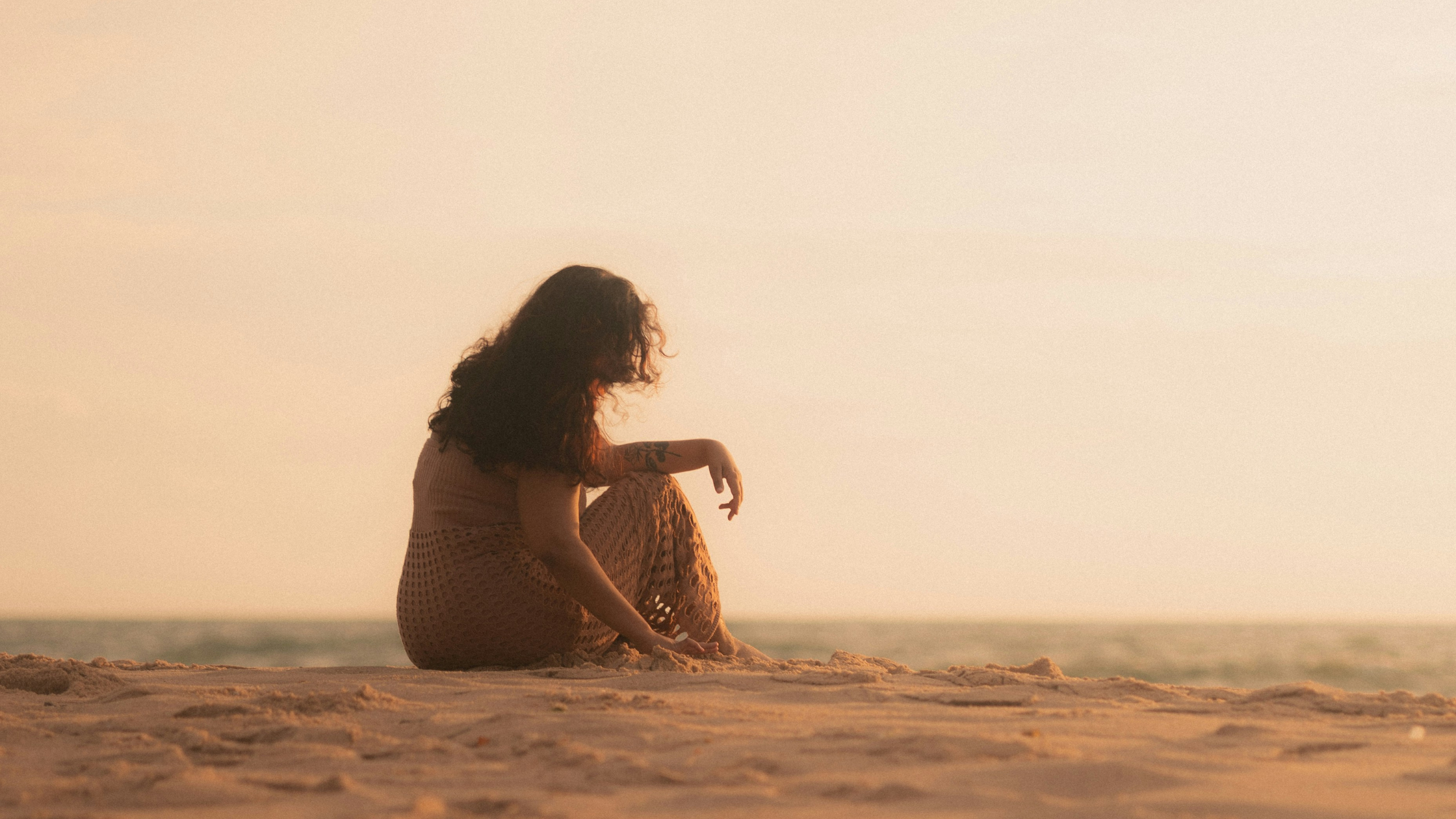 Women by herself on a beach, sitting in the sand