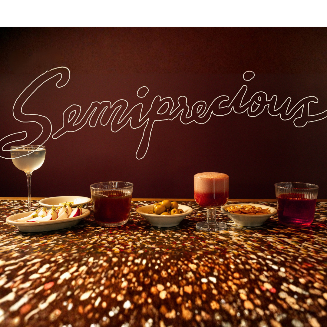 Spread of cocktails and snacks on the bar at Semiprecious with bar logo