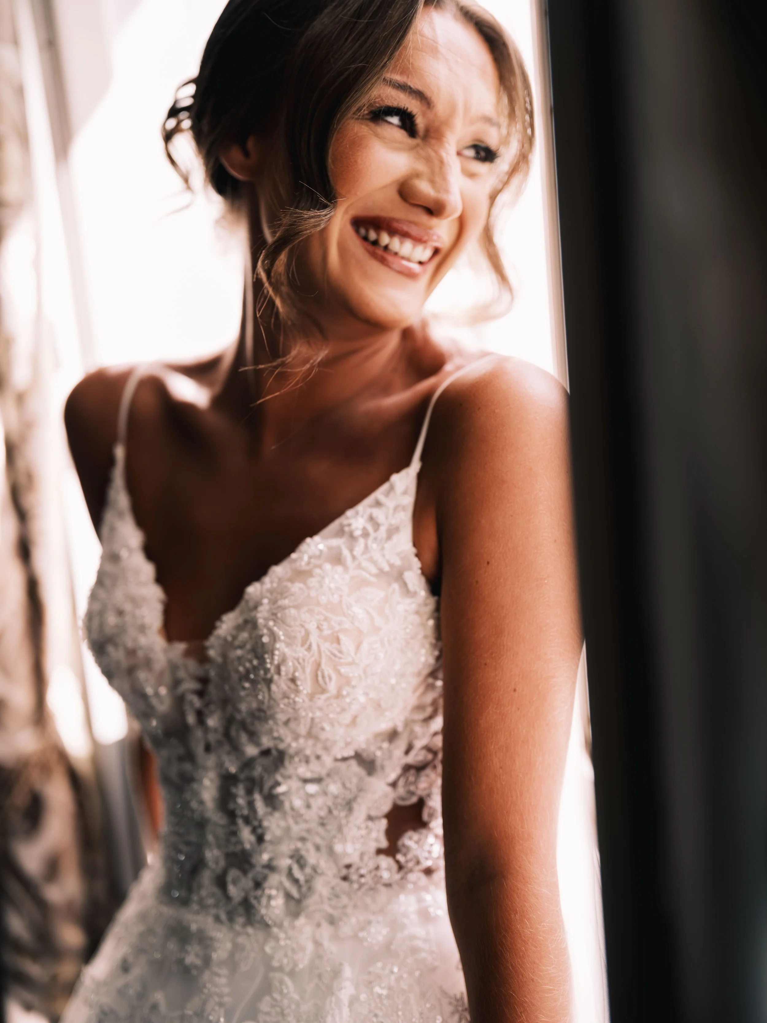 A woman smiling while wearing an elegant white wedding dress with lace details.