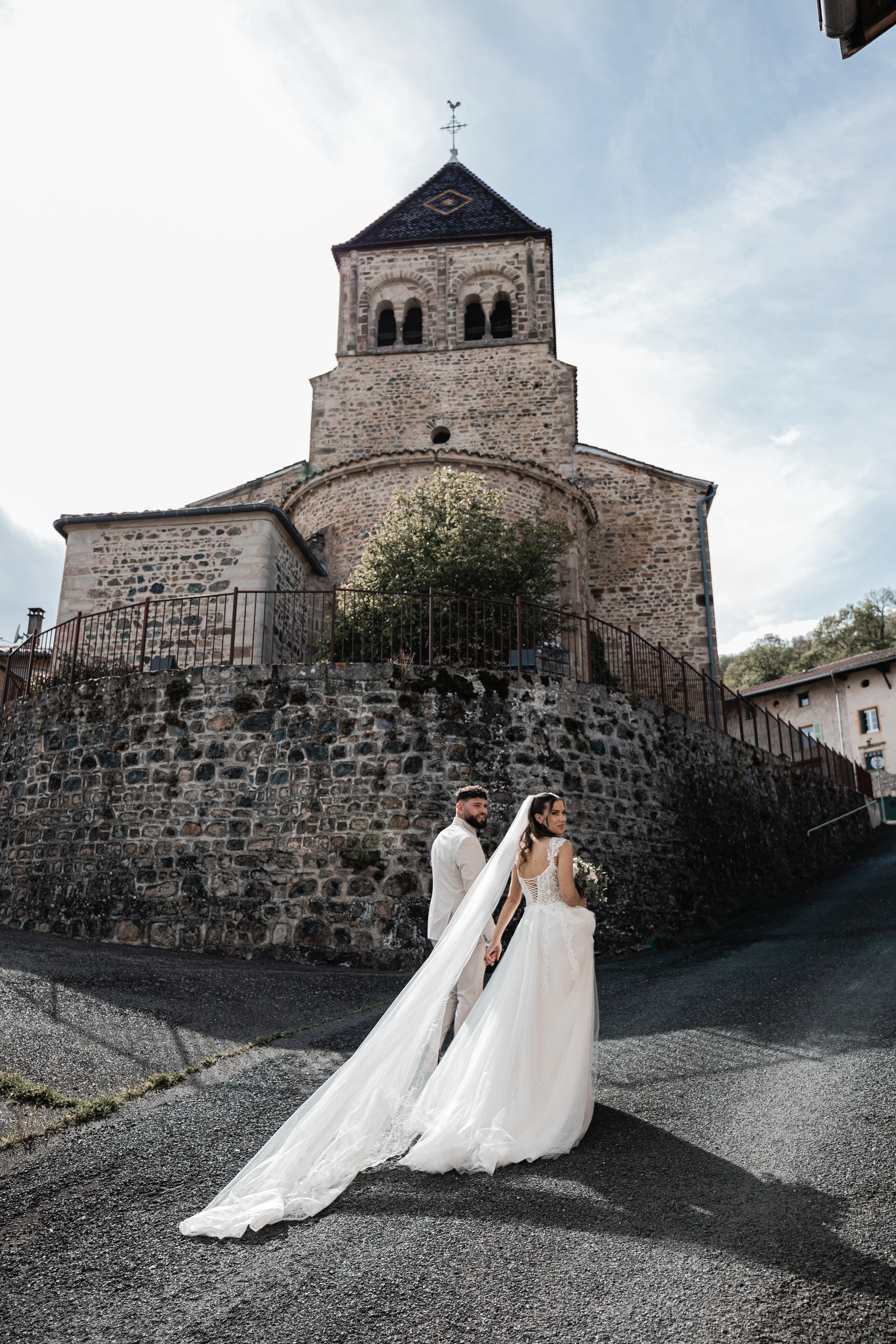 A bride and groom holding hands on a street with a historic stone church in the background.