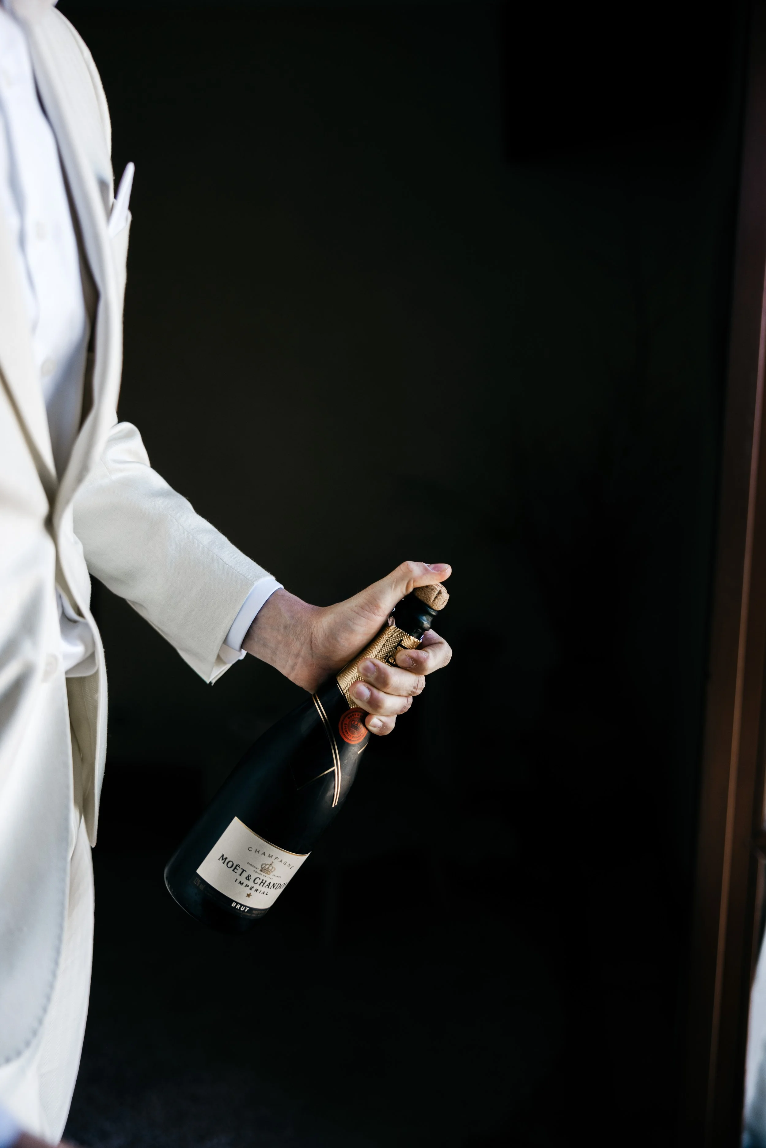 Person in a white suit holding a bottle of Moët & Chandon champagne.