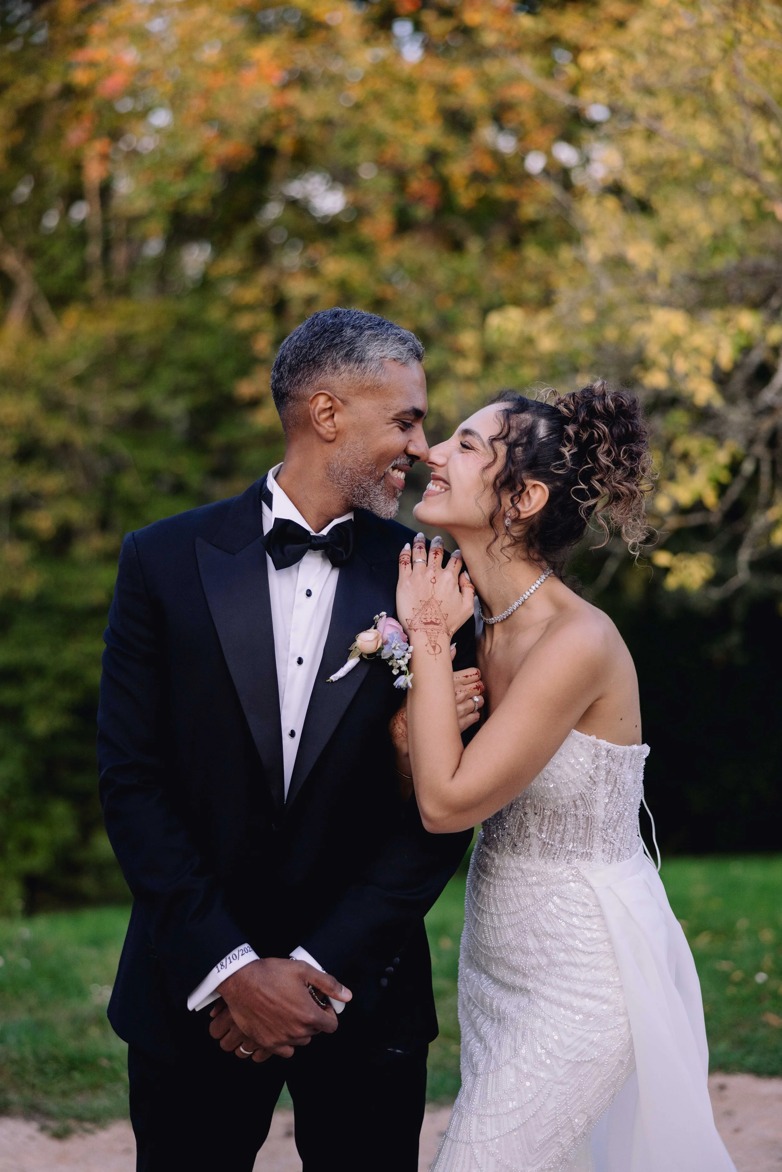 A couple dressed in wedding attire sharing a joyful moment outdoors amidst colorful autumn foliage.