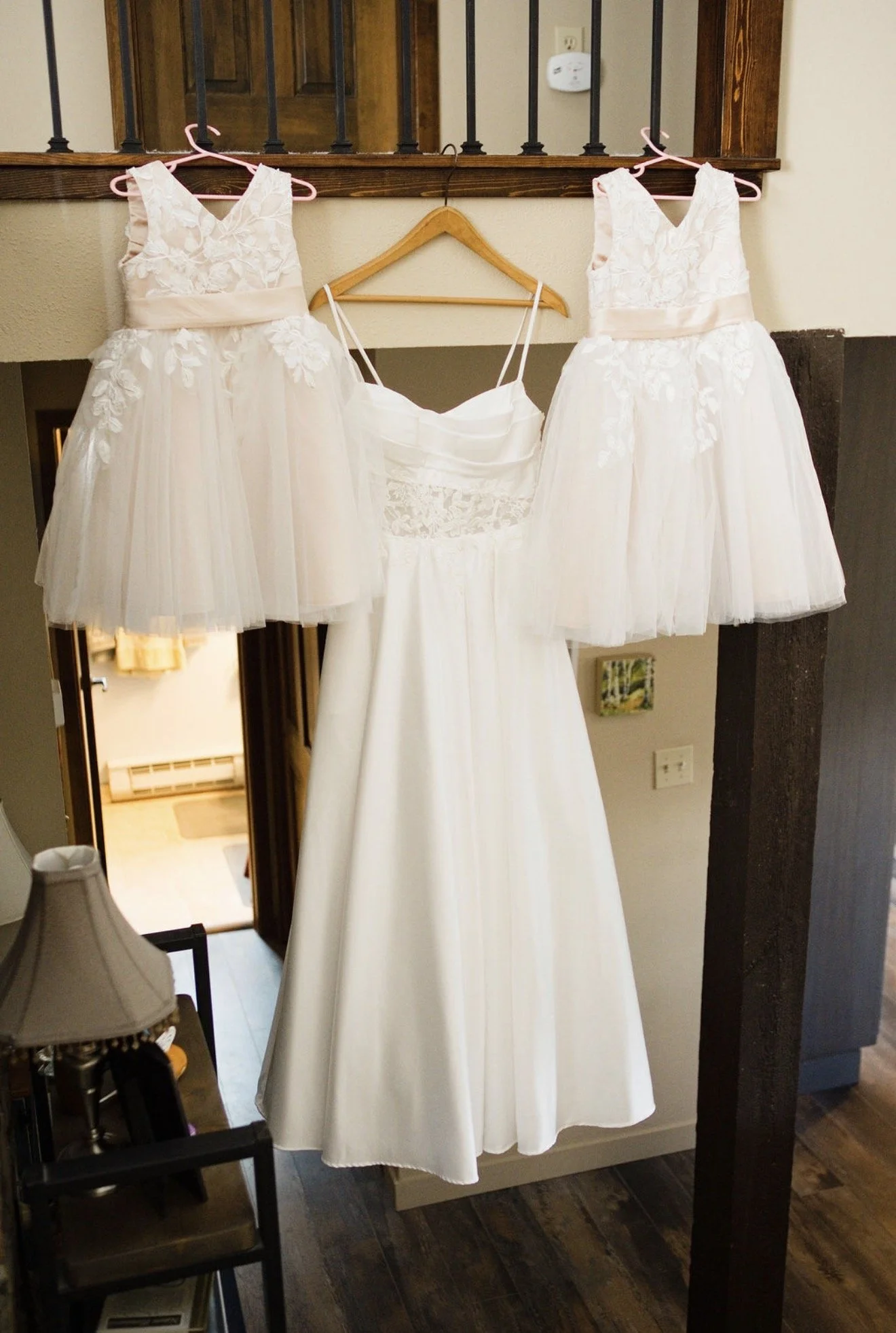 Three white dresses with lace and tulle hanging on pink hangers, and a white dress on a wooden hanger, all displayed against a wall.