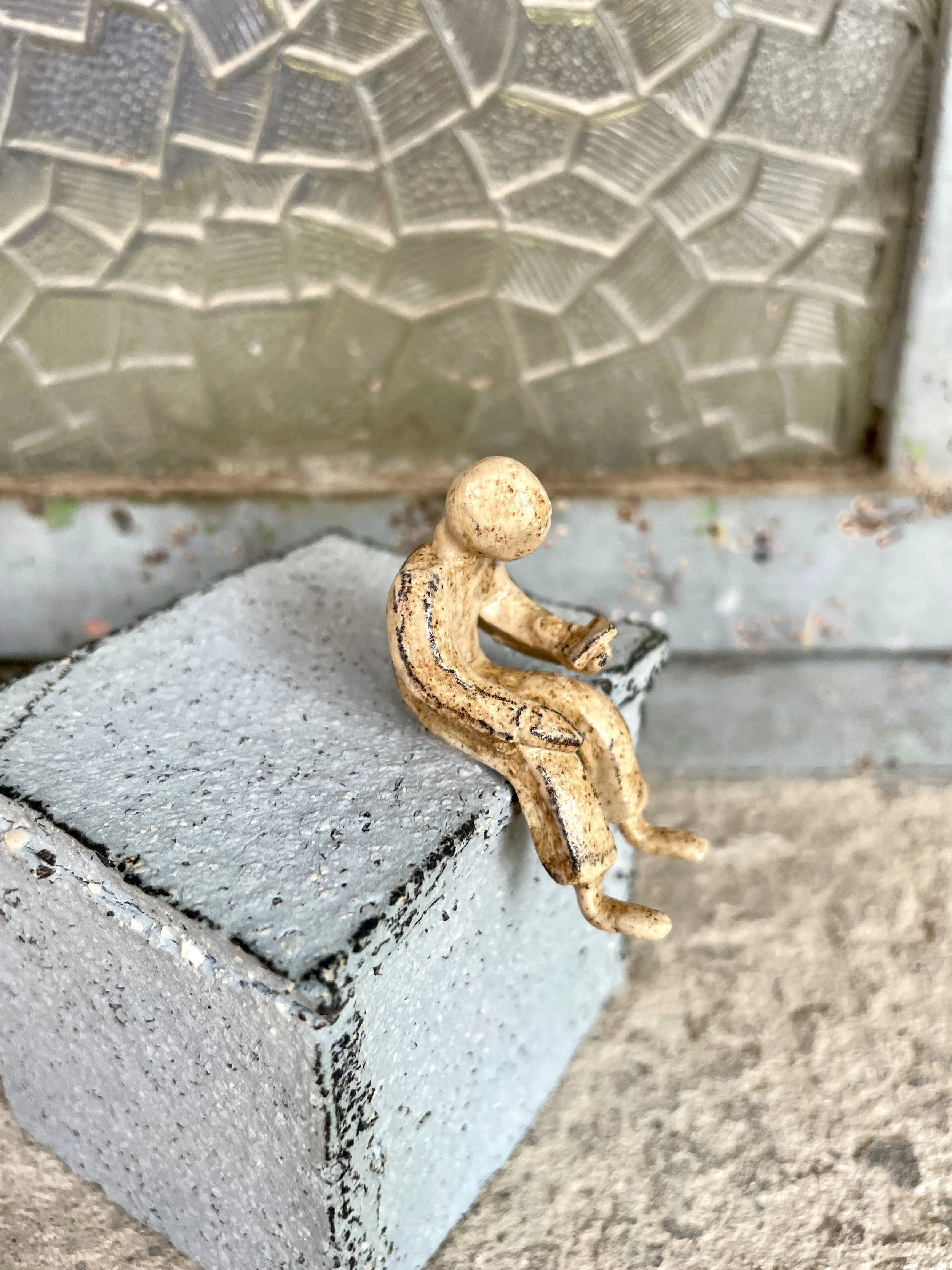 Stoneware figurine of human figure reading phone seated on pedestal.jpg