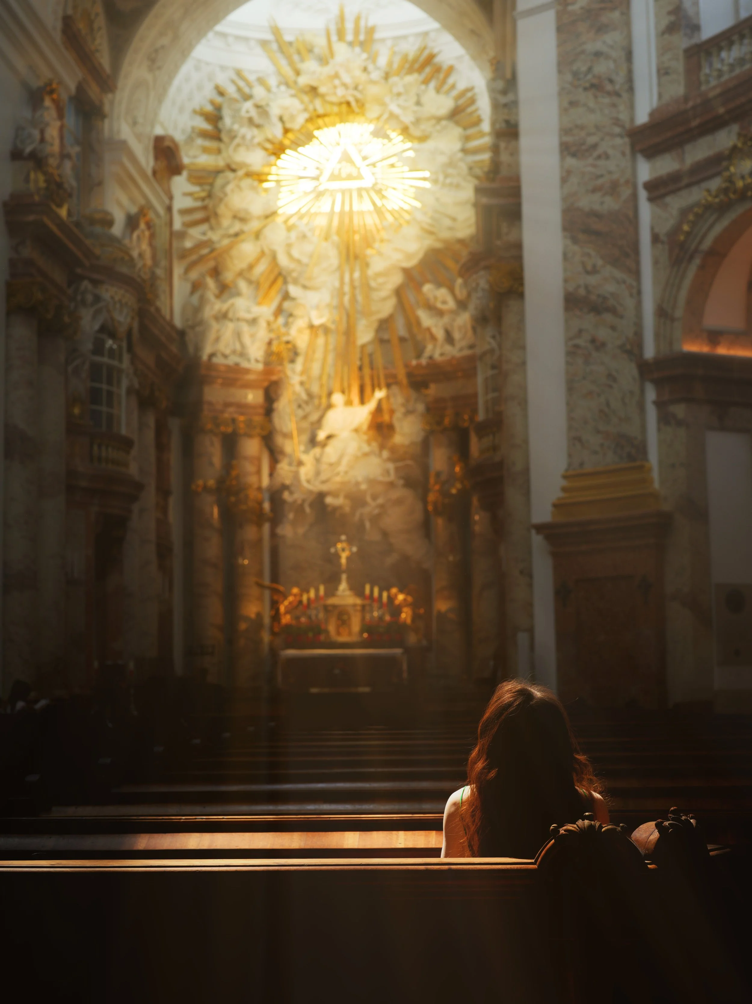 An interior of a church or cathedral with an altar, religious statues, and ornate decorations, with one person sitting on the steps in front.