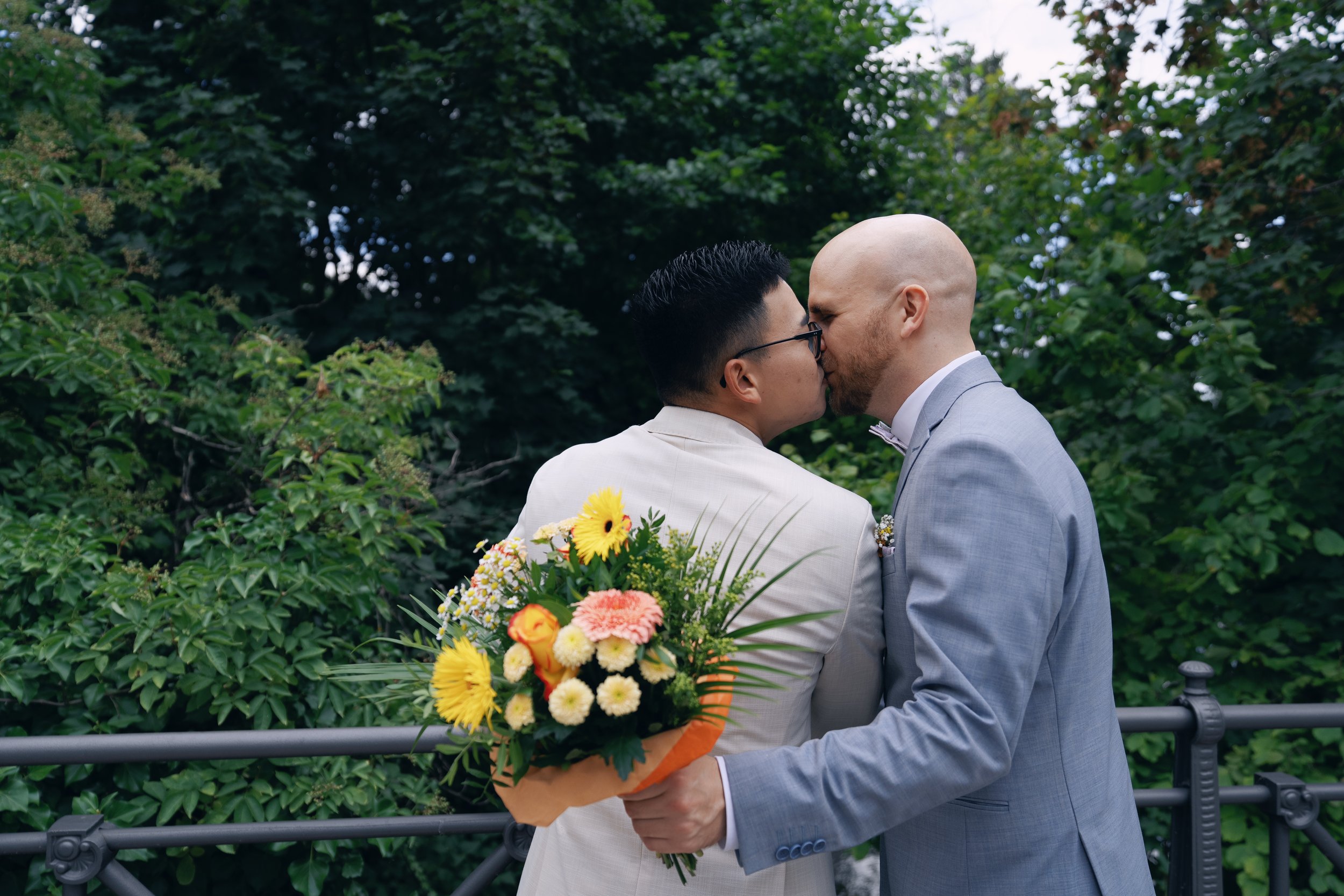Two grooms sharing a kiss in the garden after their civil wedding.