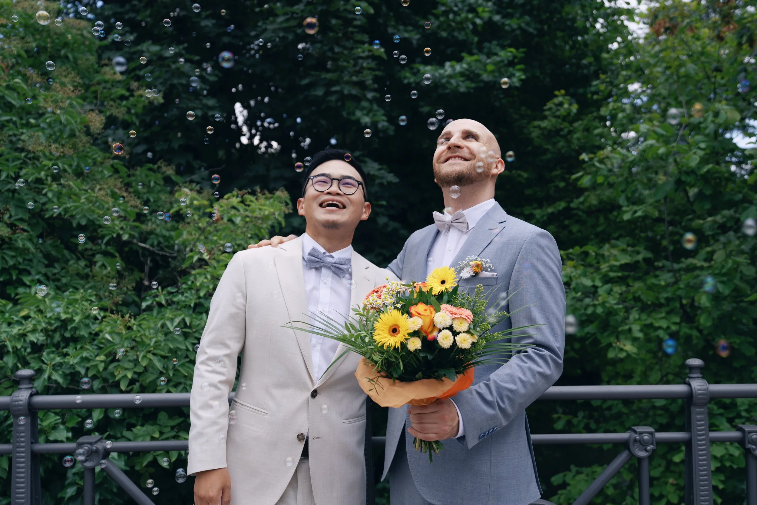Two grooms laughing together while holding their wedding bouquet.