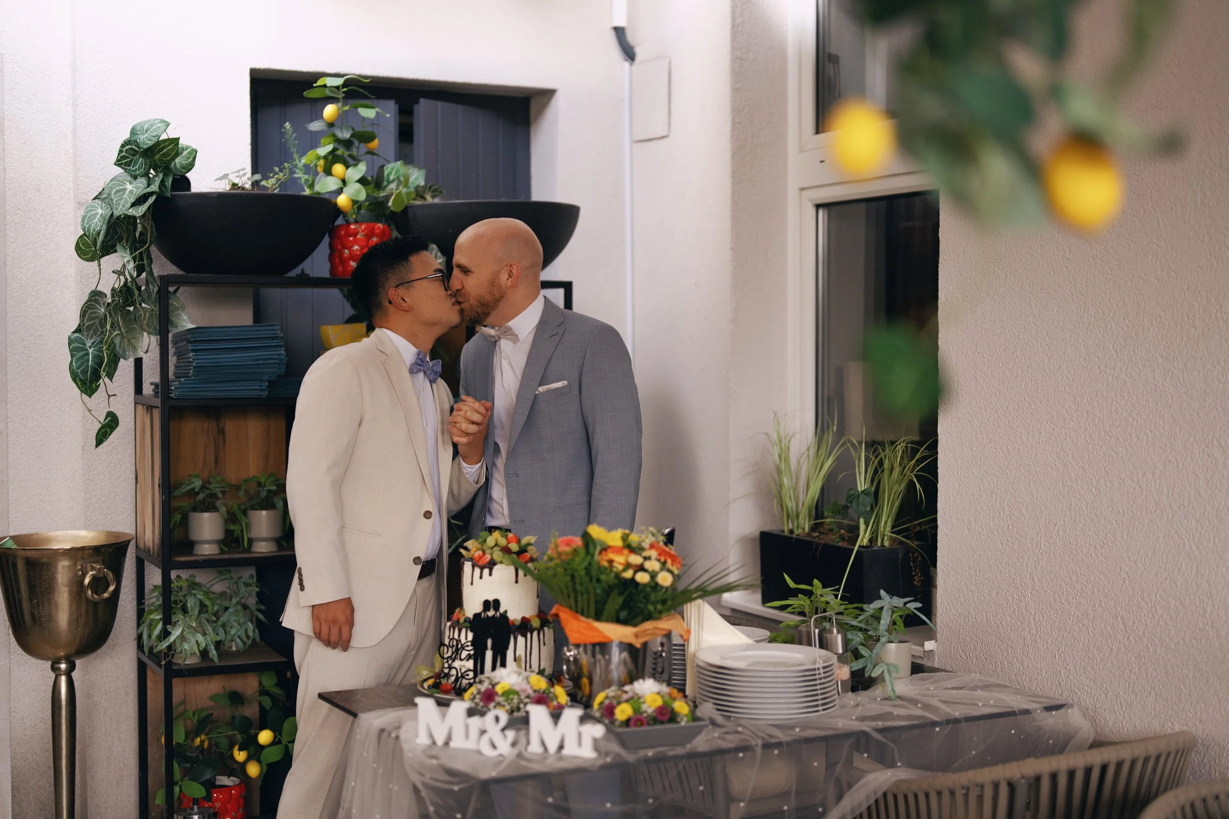 Two grooms sharing a kiss beside their wedding cake after the reception.