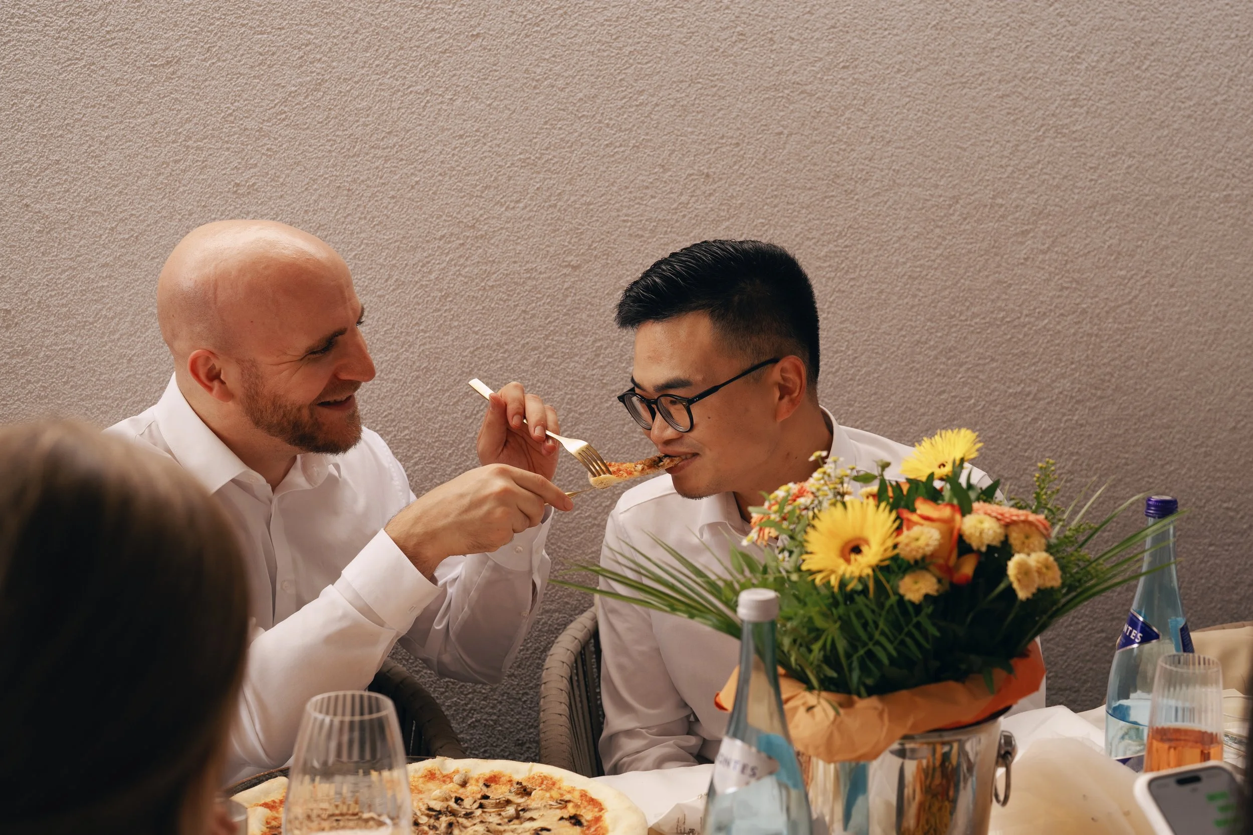 One groom feeding pizza to his husband during the wedding reception.
