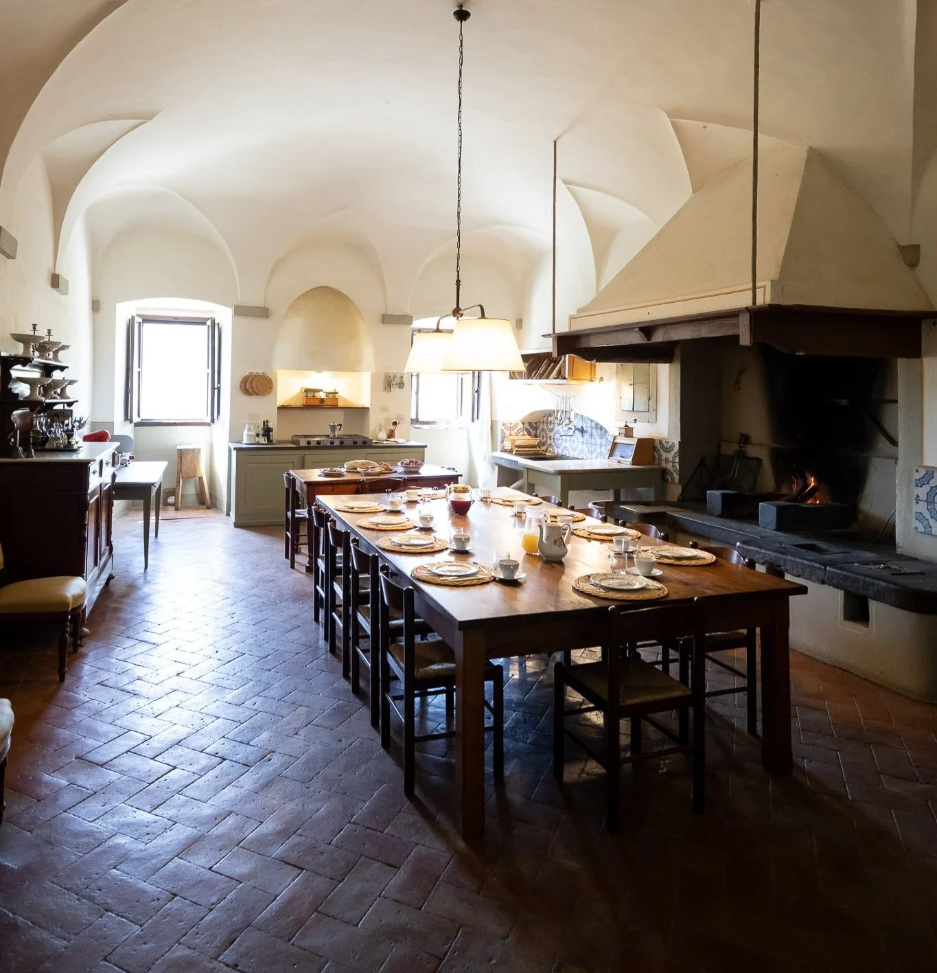Kitchen with a vaulted ceiling, long wooden dining table and large fireplace.