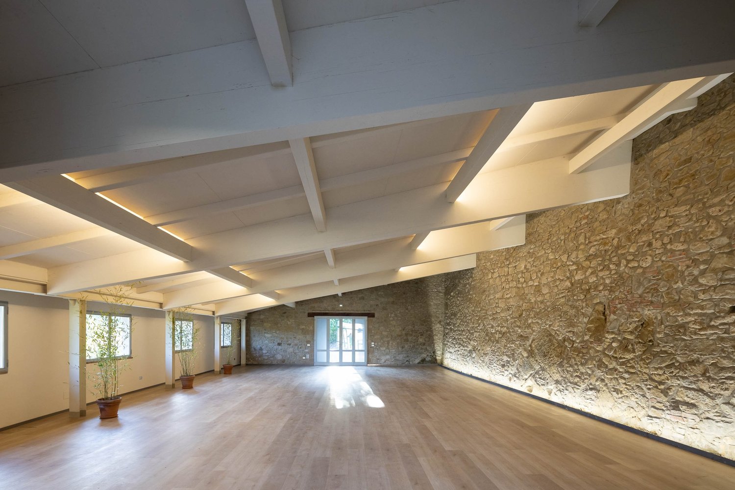 The Limonaia at Castello di Galbino, with exposed stone walls, wooden flooring and white ceiling beams.