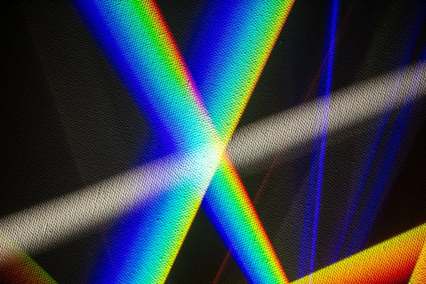 Abstract close-up of textured fabric with intersecting neon rainbow light beams on a black background