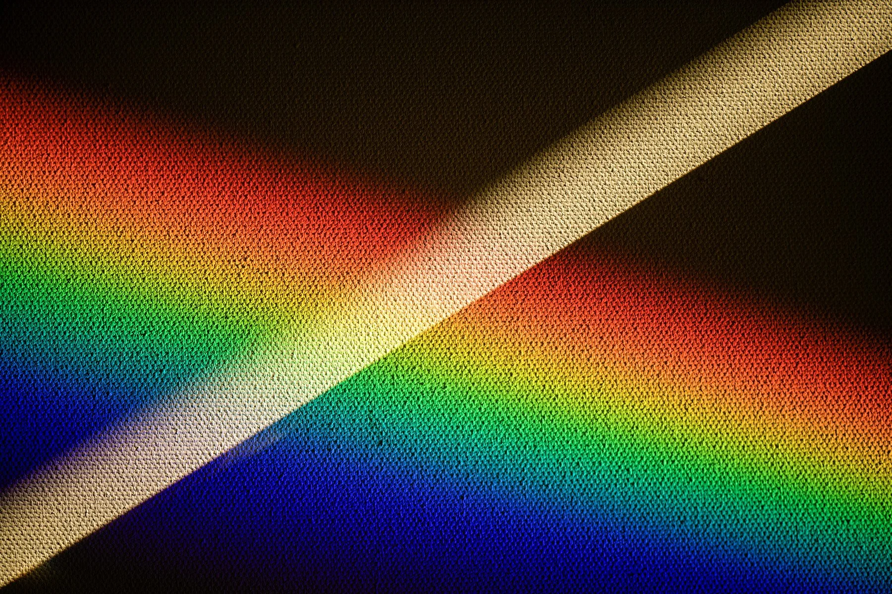 Close-up of colorful woven fabric with rainbow hues and diagonal sunlight shadows