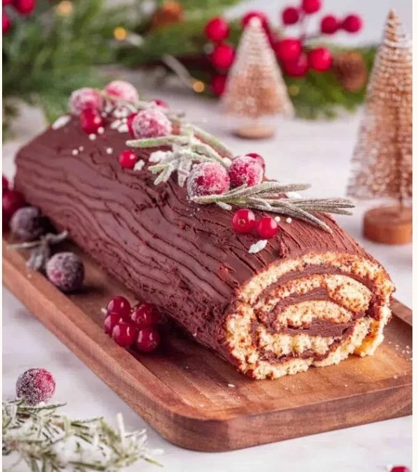 Festliche Schokoladen-Bûche-de-Noël mit Sahnefüllung, roten Beeren und Rosmarin auf einem Holzbrett