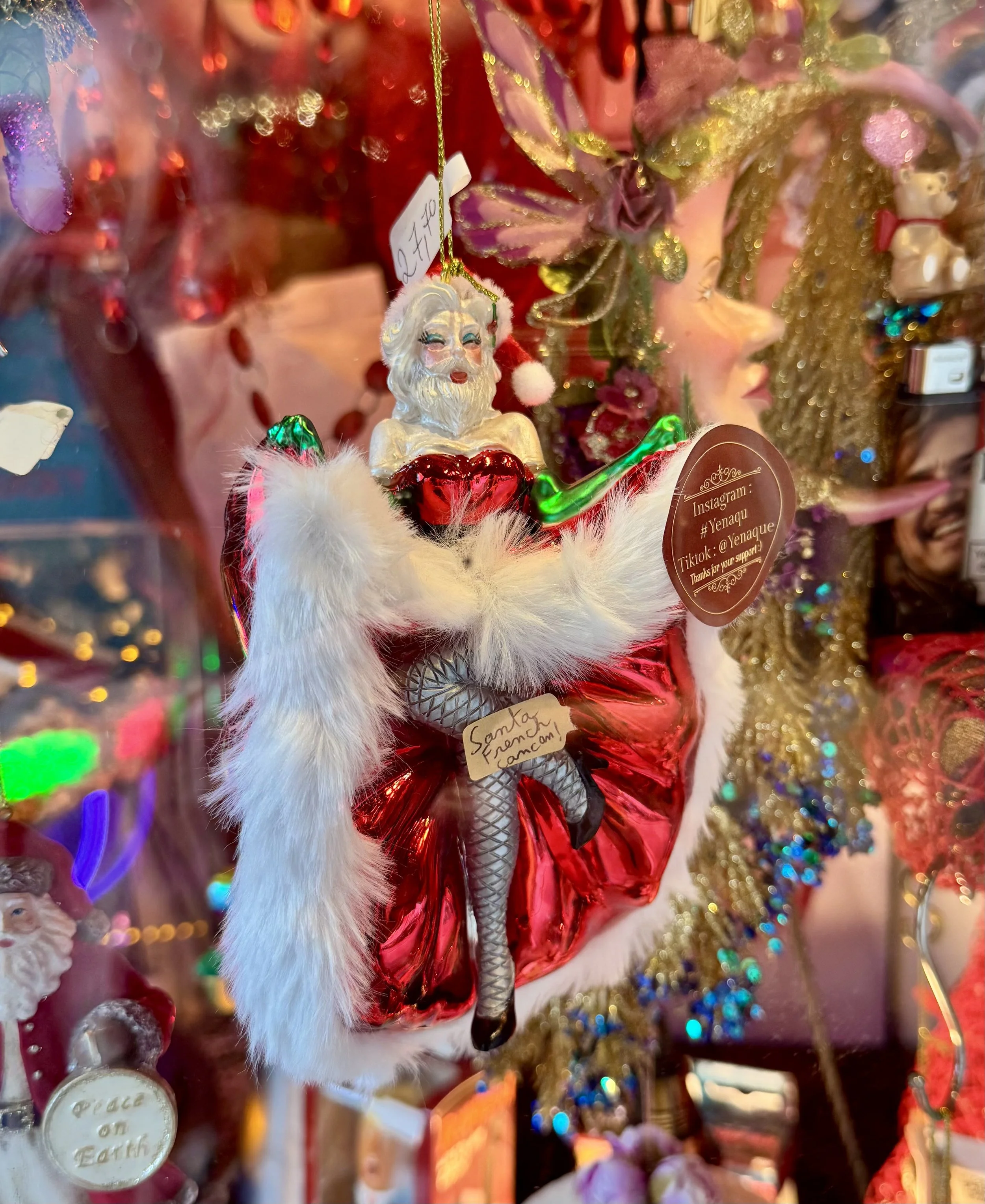 Nahaufnahme eines glitzernden Weihnachtsmann-Ornaments in rotem Gewand zwischen farbenfrohen Weihnachtsdekorationen und Lichterketten.