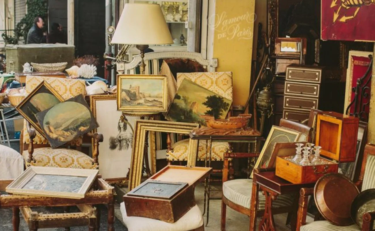 A collection of antique furniture and framed paintings at an outdoor flea market or antique shop.