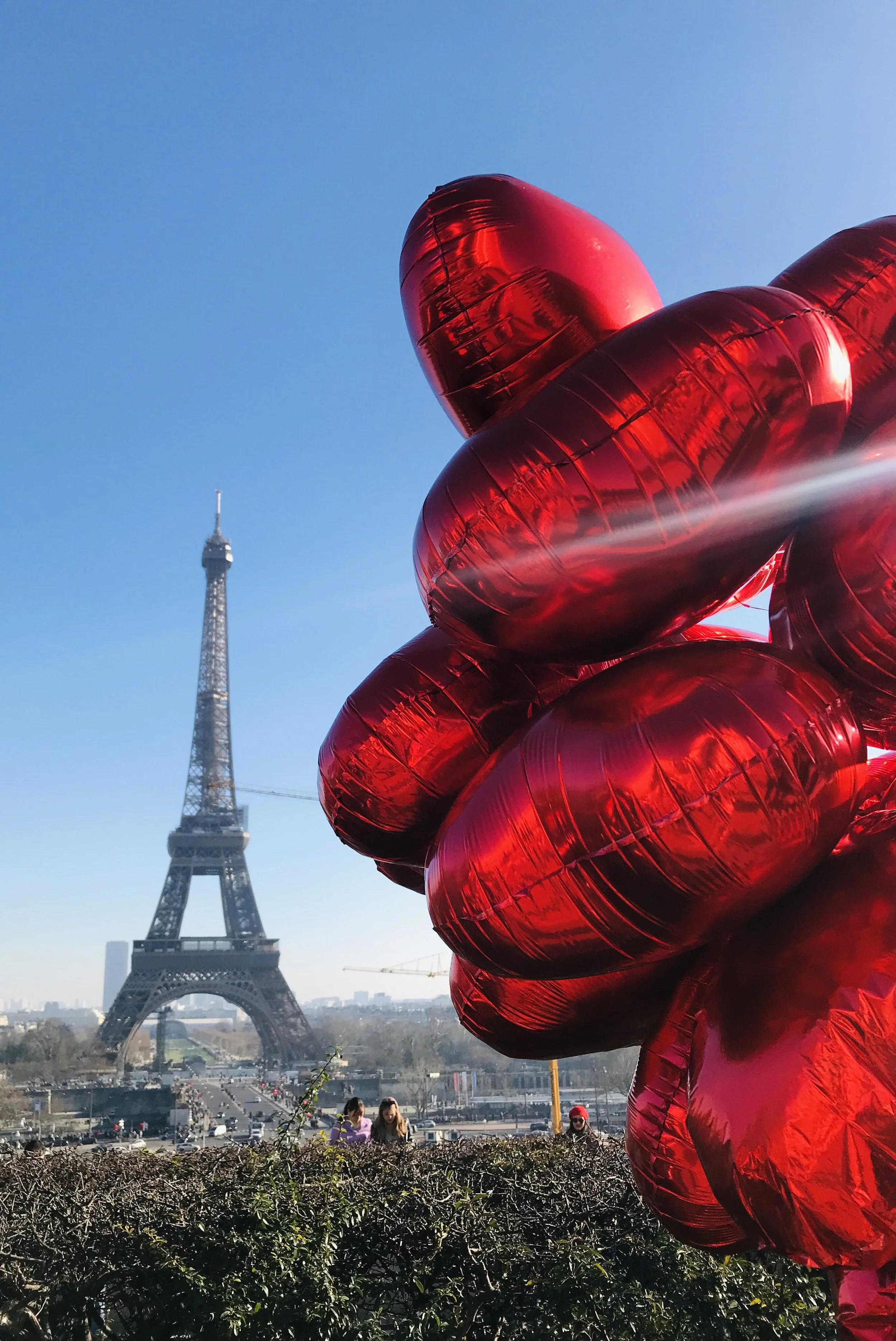 Red heart-shaped balloons in front of the Eiffel Tower on a clear day.