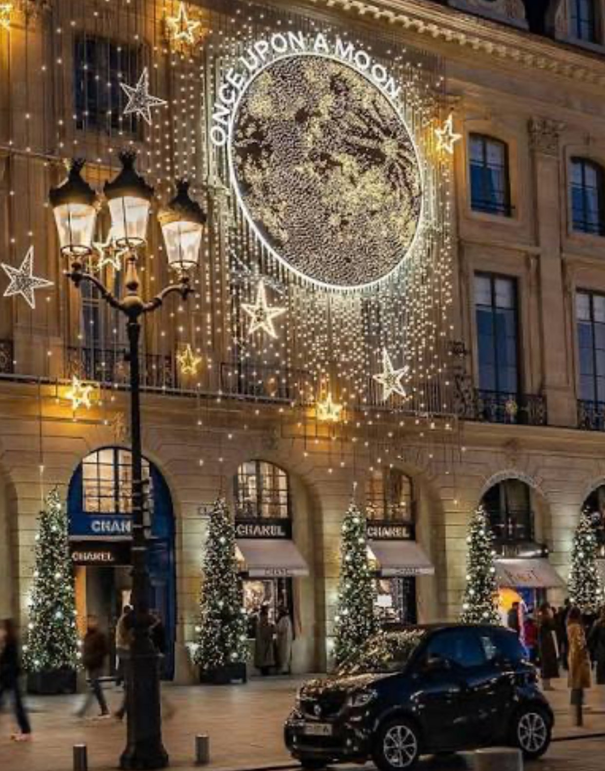 Weihnachtlich beleuchtete Fassade des Kaufhauses Galeries Lafayette mit Lichtervorhang, Sternen und geschmückten Tannenbäumen bei Nacht.