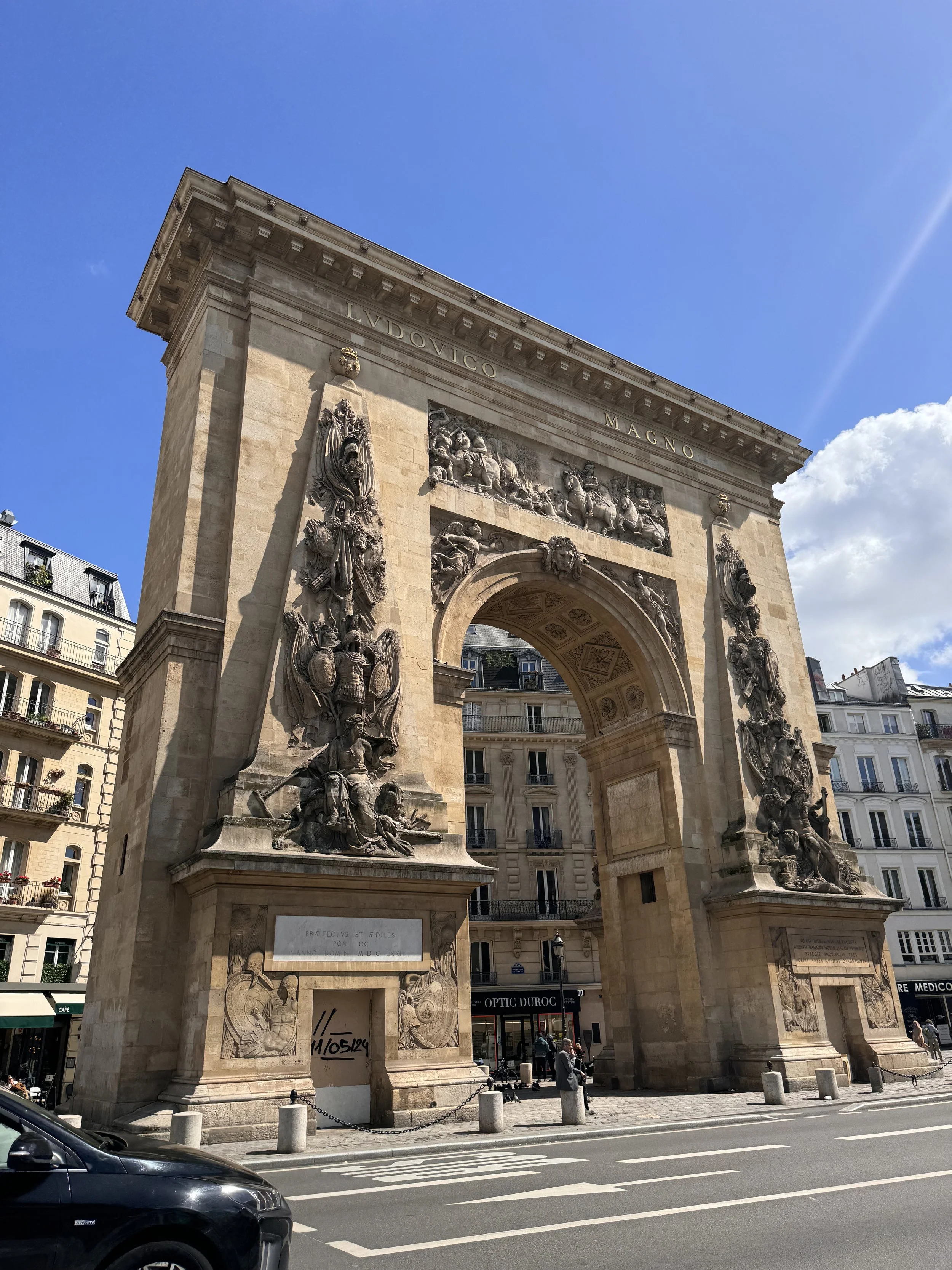 The Arc de Triomphe in Paris, France, with detailed sculptures and inscriptions, set against a blue sky with some clouds.