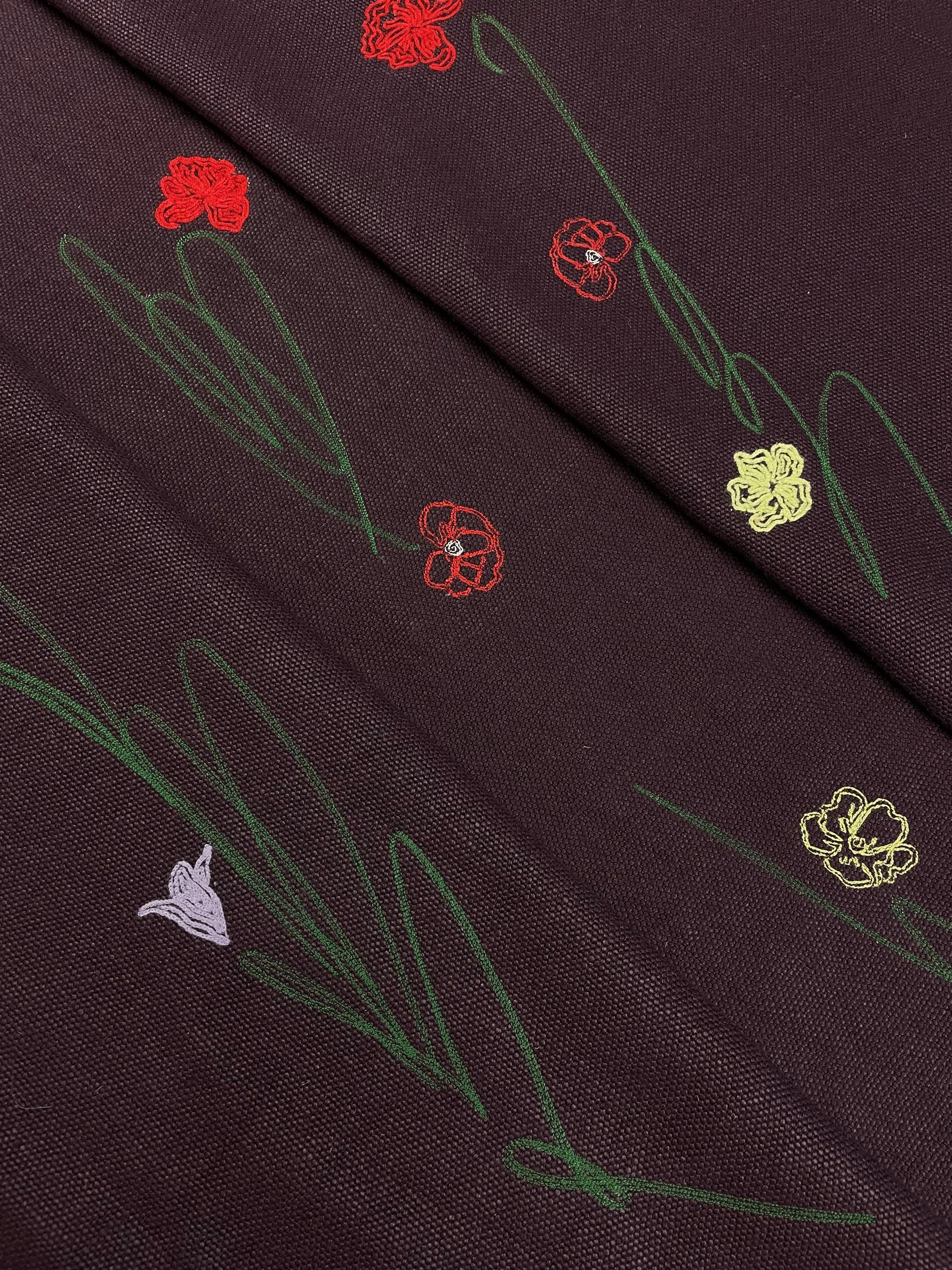 Close-up of dark fabric with embroidered flowers and green stems.