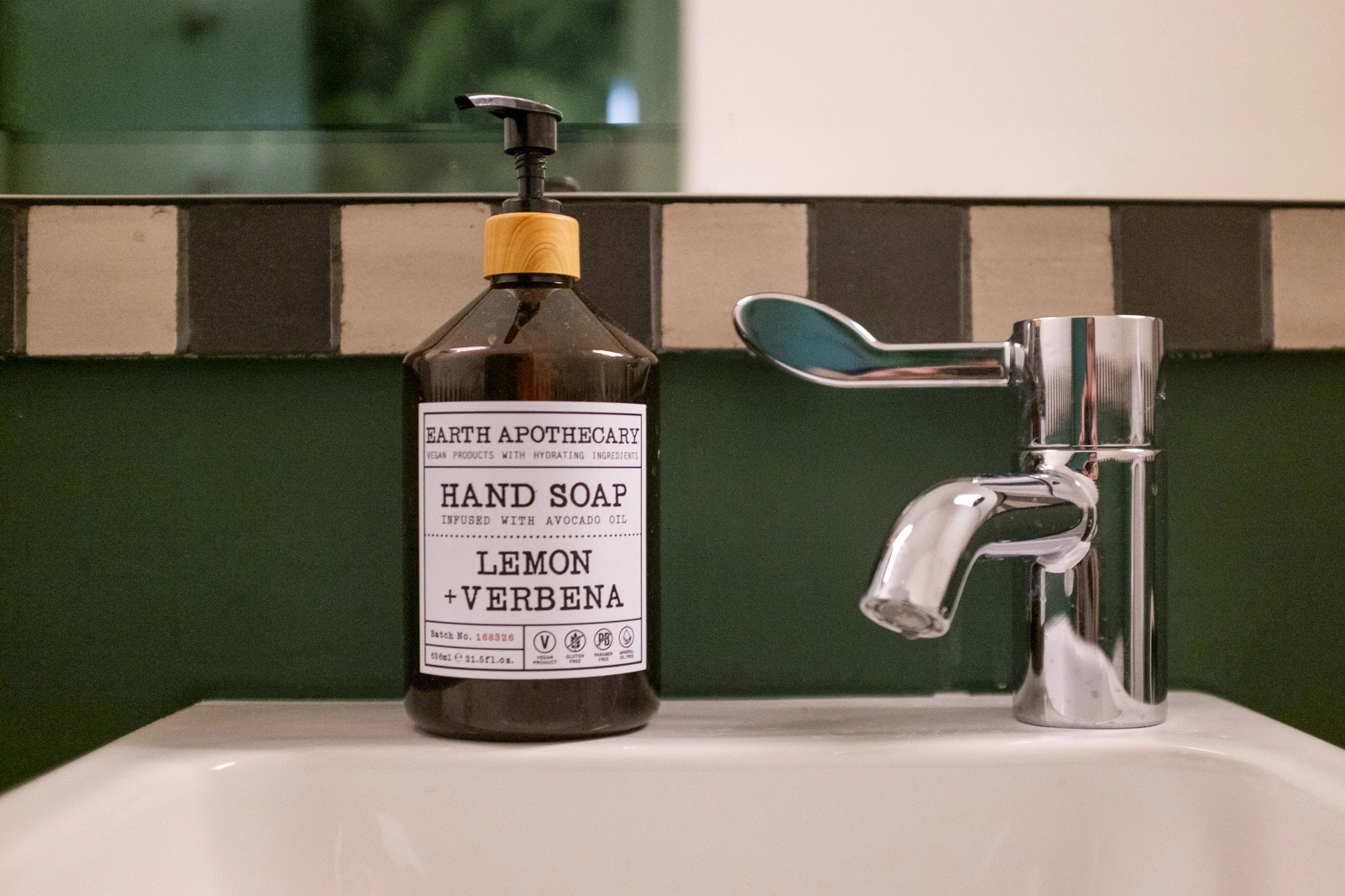 Bottle of Earth Apothecary Lemon Verbena hand soap with a pump dispenser on a bathroom sink next to a metal faucet.