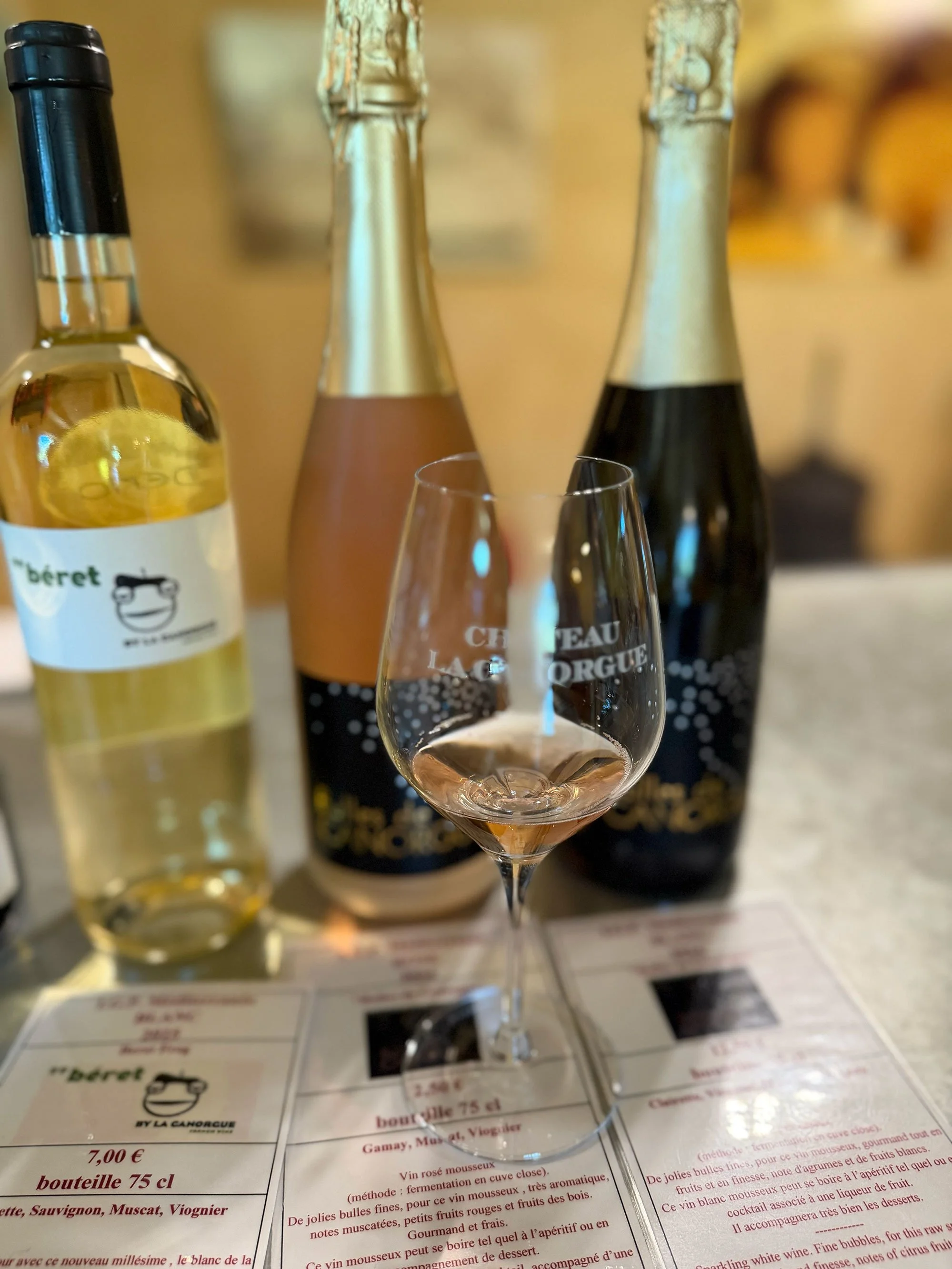 A glass of sparkling rosé wine surrounded by bottles of champagne and white wine on a restaurant menu table.