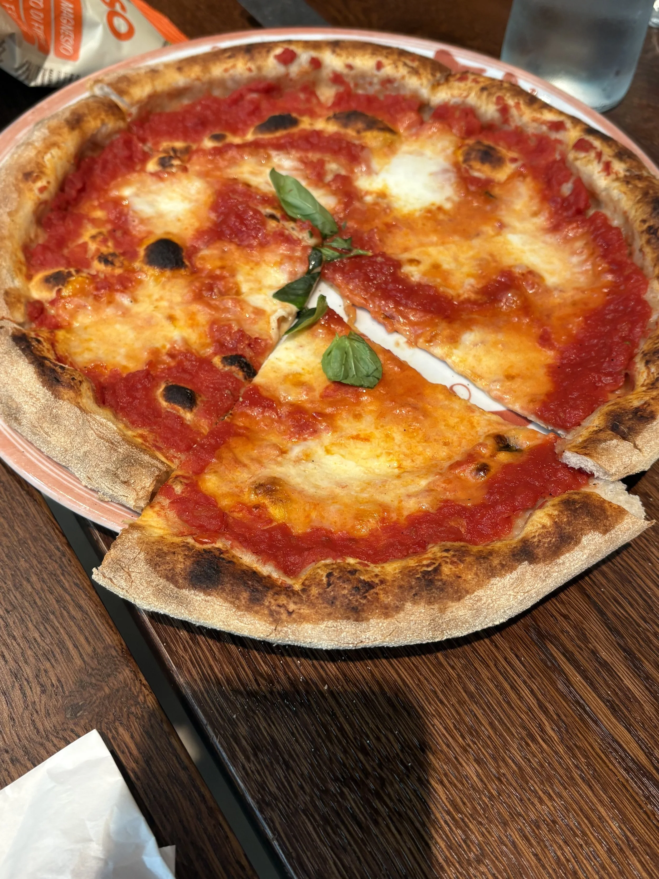 A Margherita pizza with tomato sauce, mozzarella cheese, basil leaves, and a toasted crust on a plate.