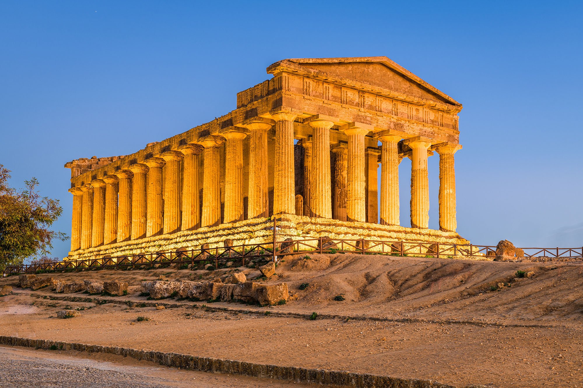 Ancient Greek temple ruins illuminated at sunset, featuring tall columns and a triangular pediment, in a historical site.