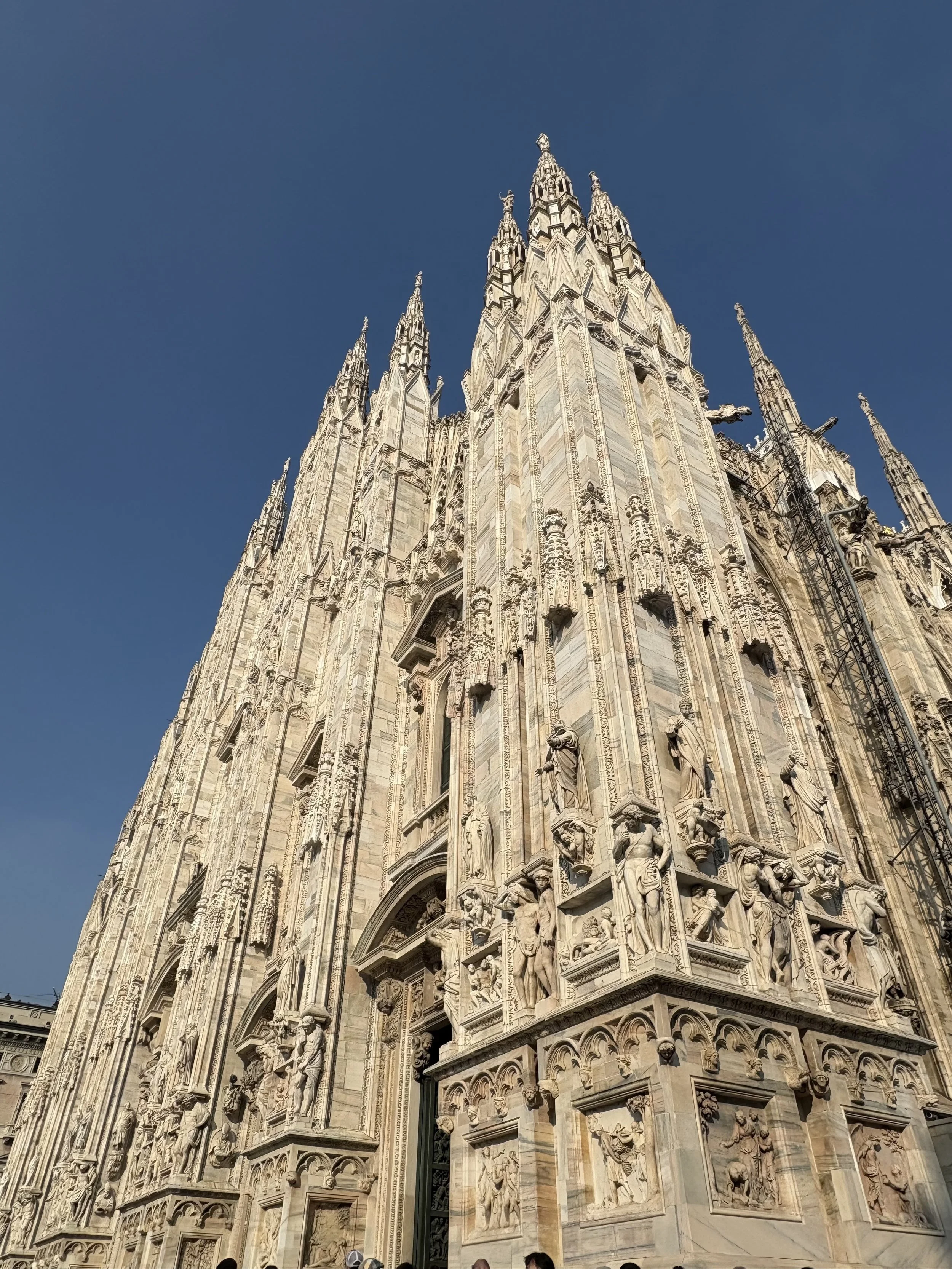 Close-up view of the intricate stone exterior of a Gothic cathedral with sculptures and tall spires reaching into a clear blue sky.