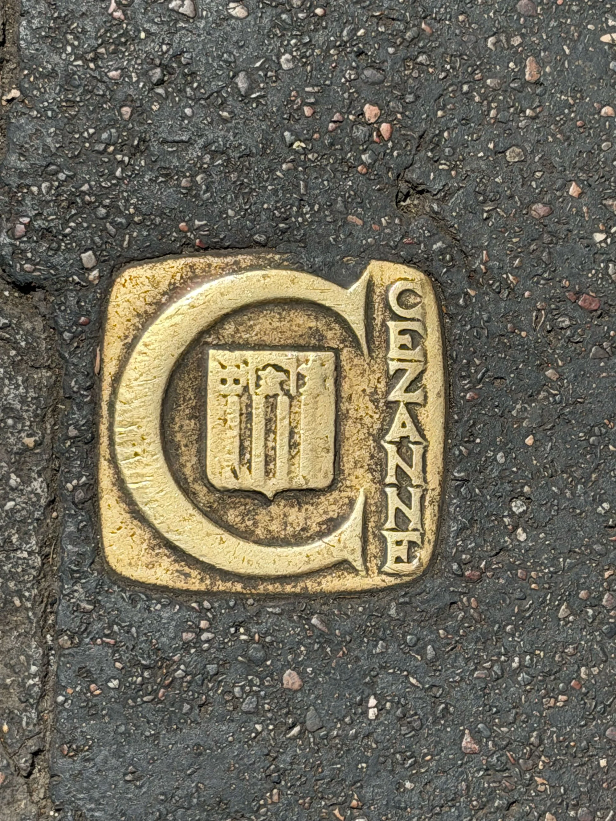 A metal street drain cover embedded in an asphalt street with the word 'DRAIN' written on it.