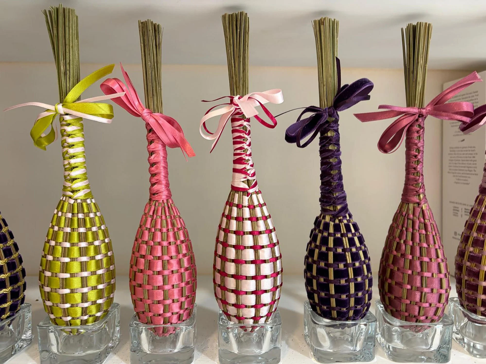 Colorful decorative bundles wrapped with ribbons in pink, purple, yellow, and green, arranged in small glass containers.