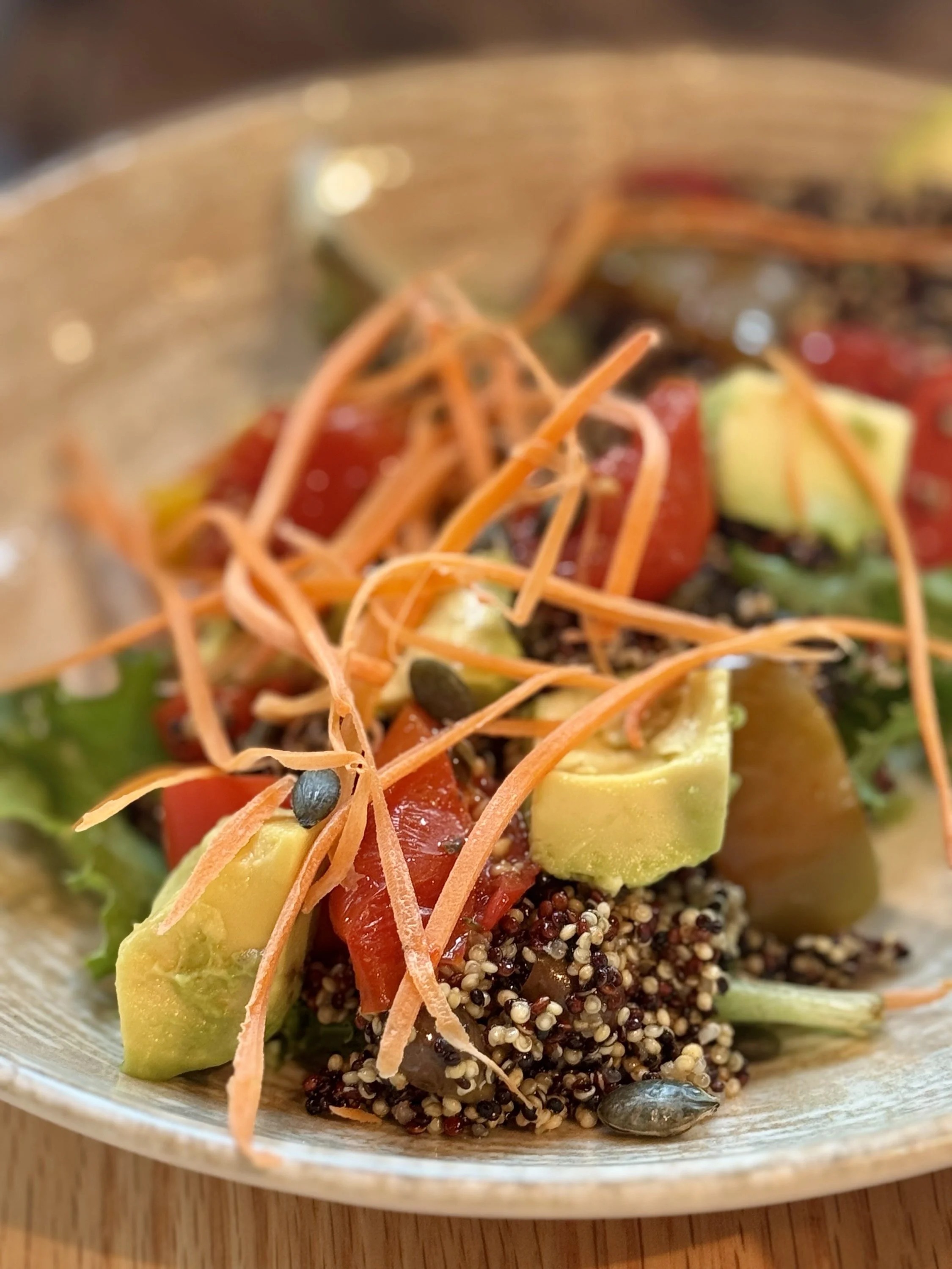 Close-up of a bowl of salad with shredded carrots, avocado chunks, cherry tomatoes, and quinoa, served in a rustic bowl.