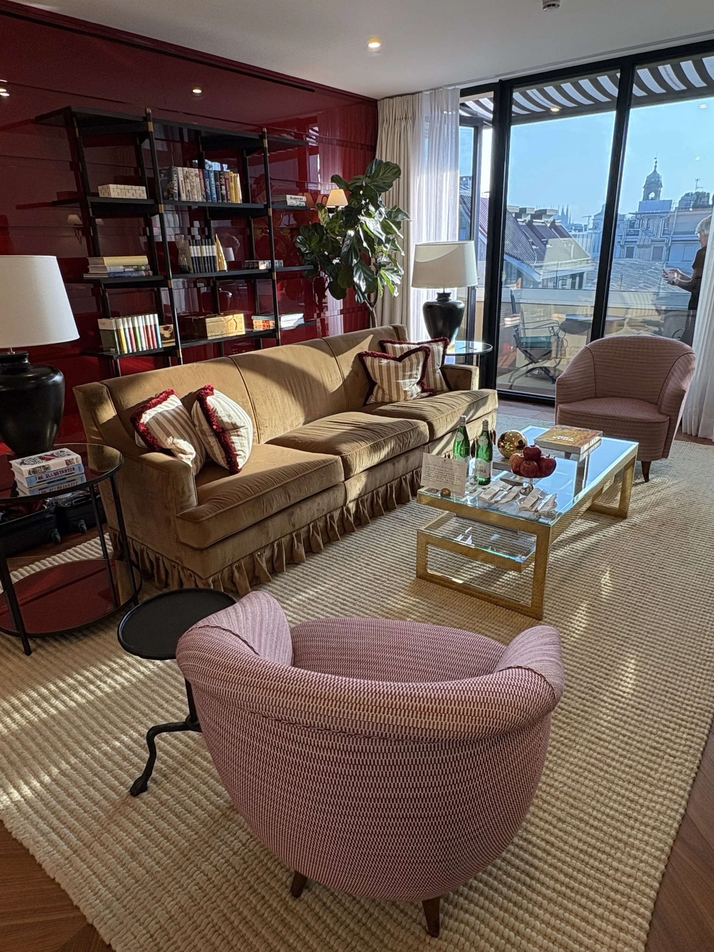 Living room with a beige sofa, pink armchair, glass coffee table, and door to balcony with city view.