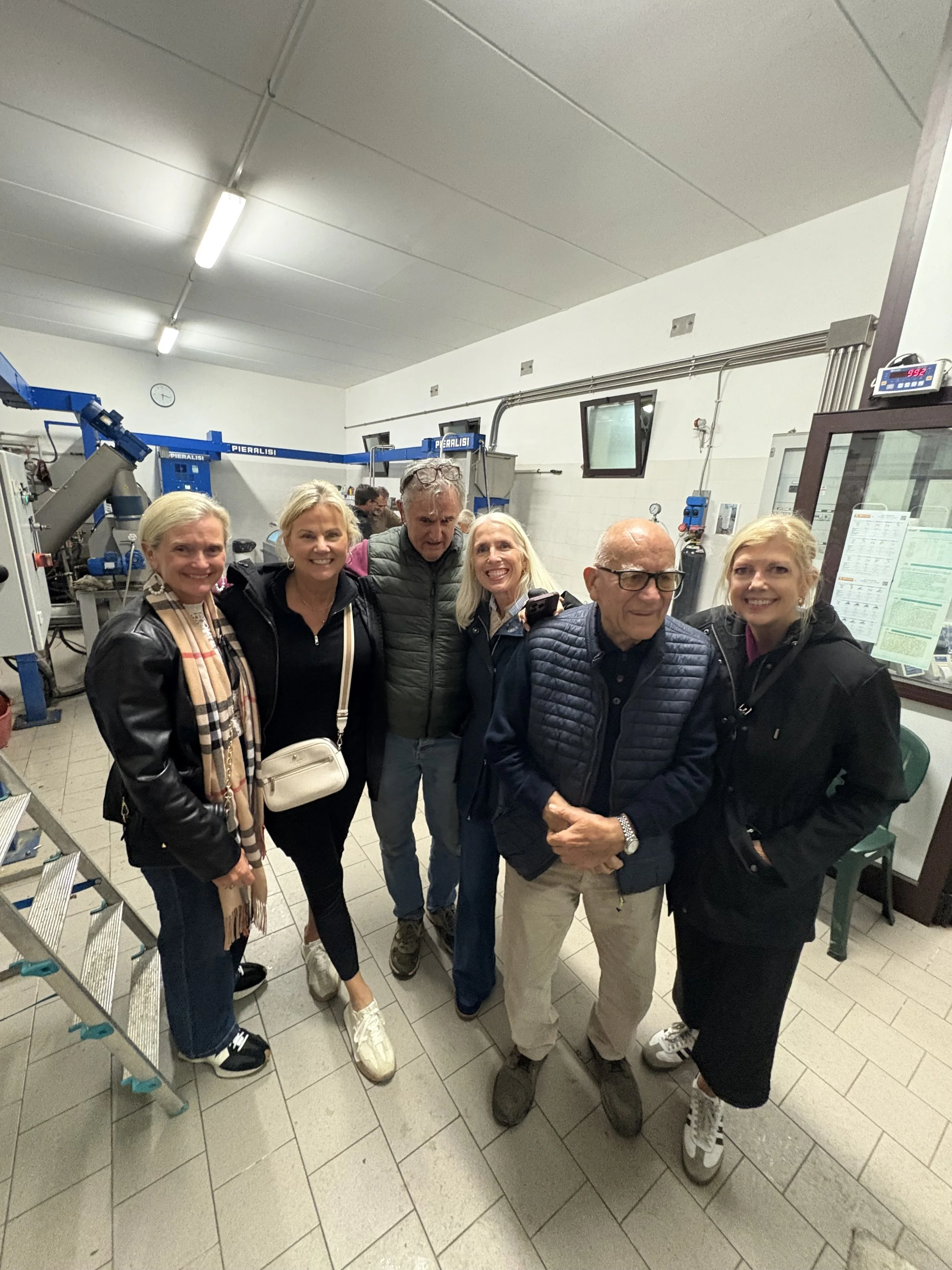 Group of seven people standing inside a machinery workshop or lab, with industrial machines and equipment visible in the background.