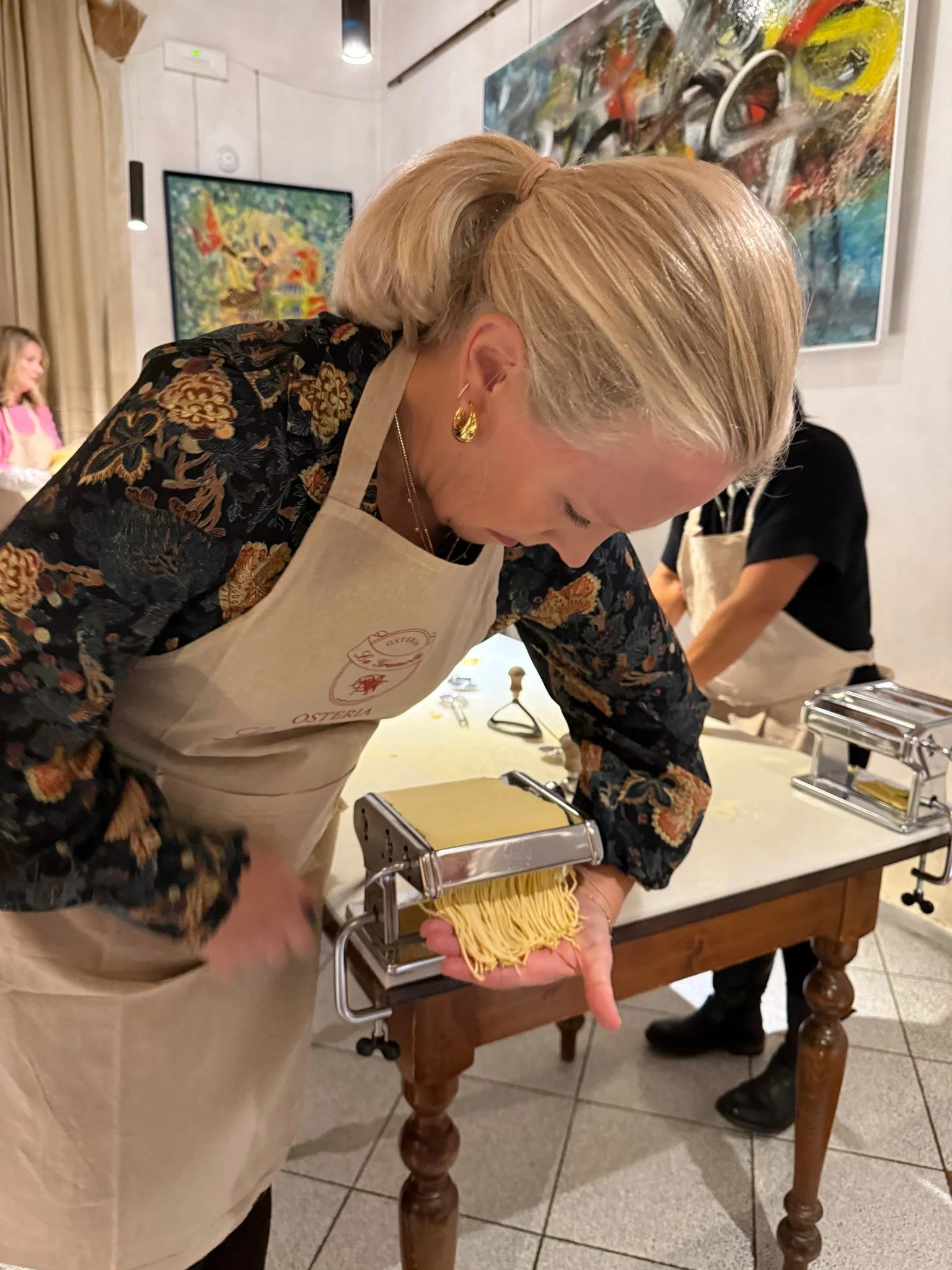 Woman using a pasta machine to make fresh pasta in a kitchen or cooking class setting.