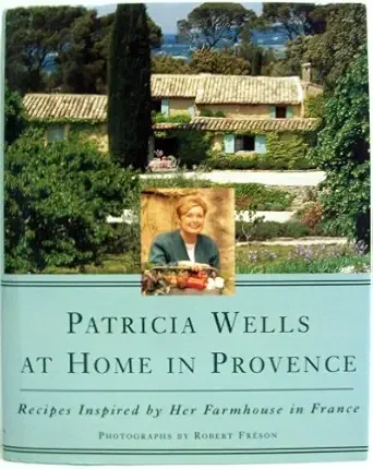 A book cover titled 'Patricia Wells at Home in Provence' with a subtitle about recipes inspired by her farmhouse in France, featuring a photo of Patricia Wells holding a basket of vegetables, surrounded by greenery and farmhouse buildings.
