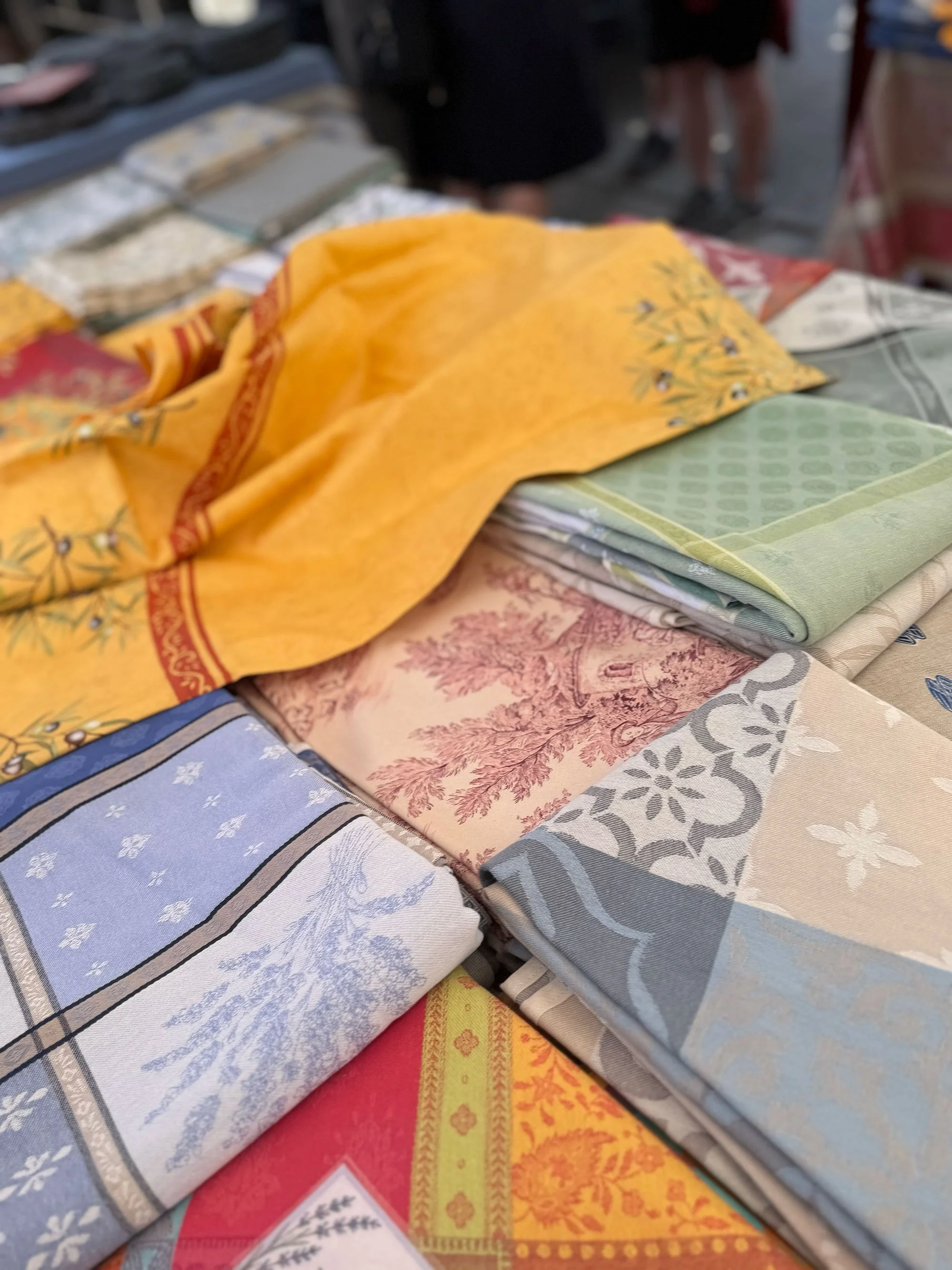 Various folded patterned towels or fabrics displayed on a table at a market.