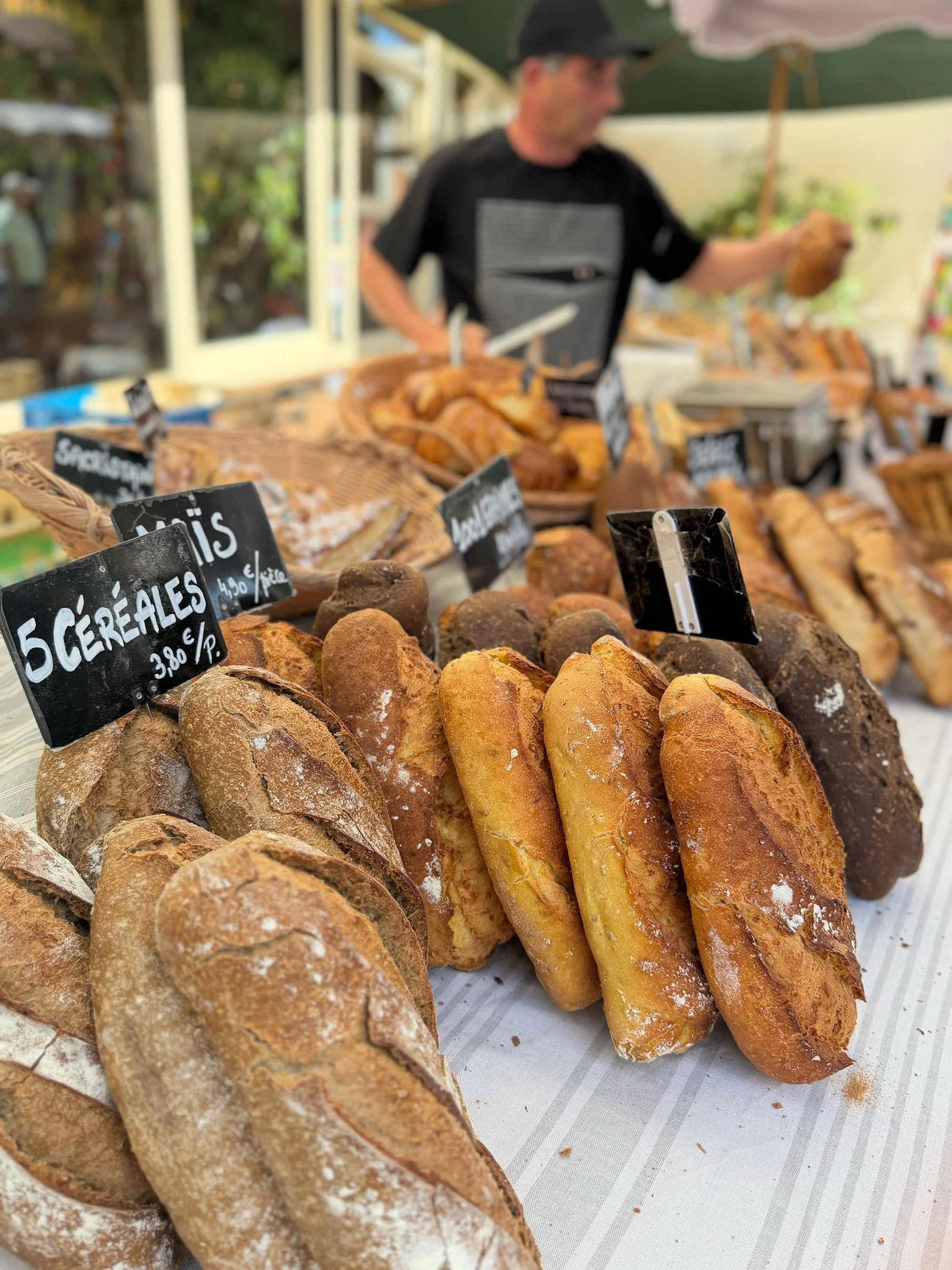Various types of fresh bread and baked goods on display at a market stall, with black price tags.