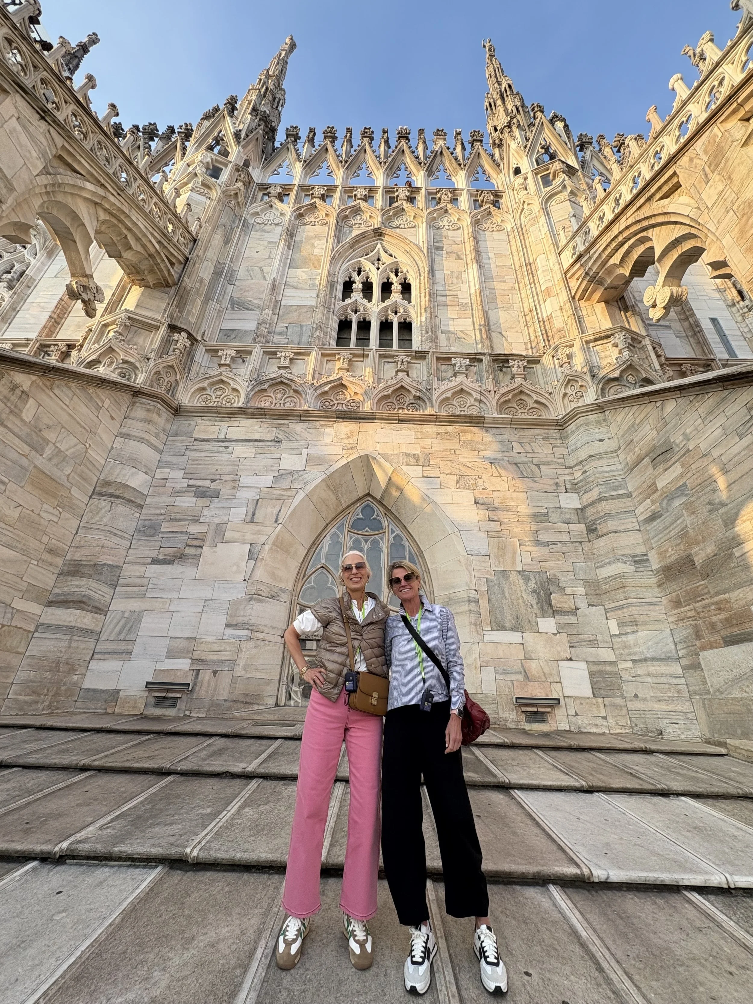 Two women standing in front of a cathedral with detailed Gothic architecture and tall spires, smiling and posing for the photo.