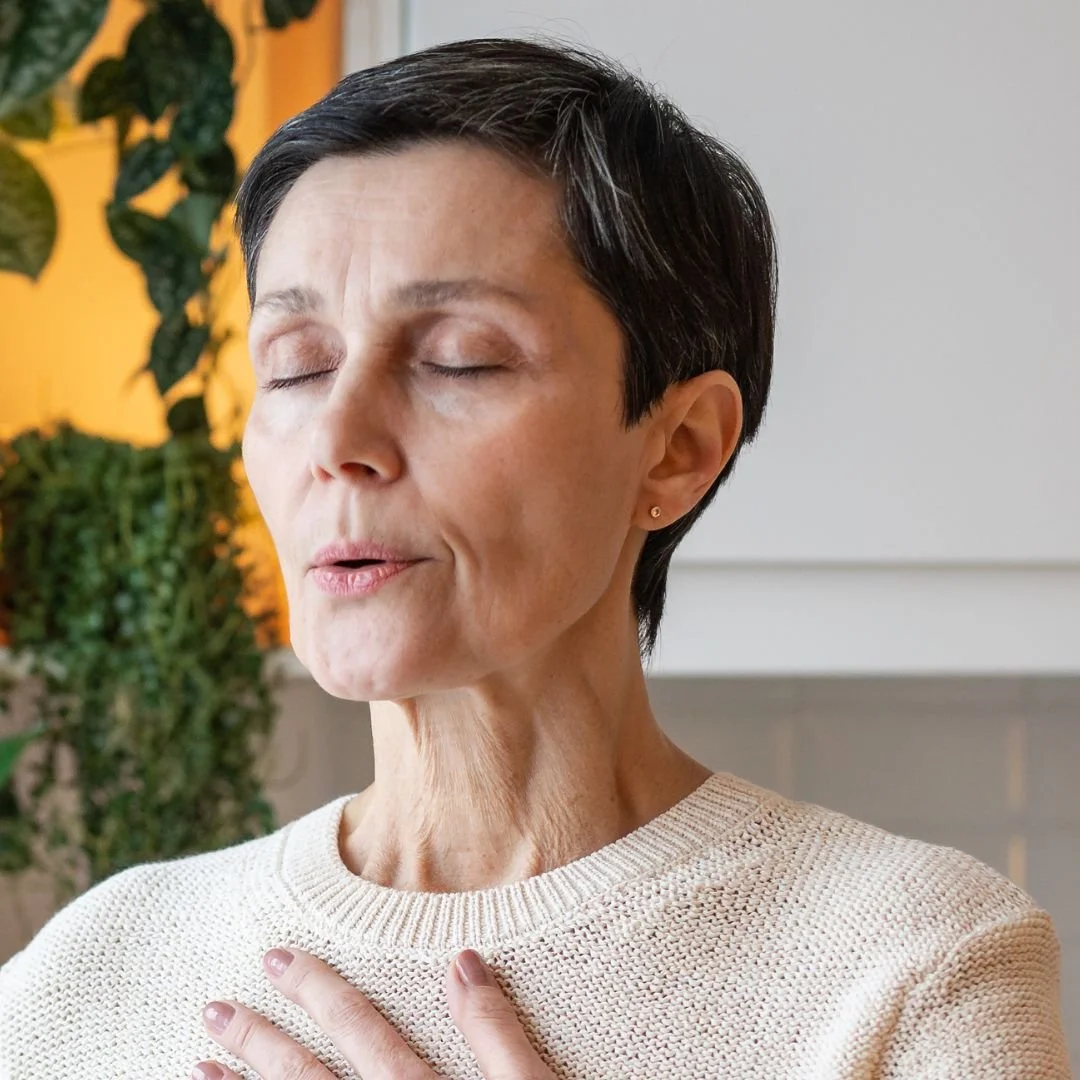 Woman breathing in a cream jumper with one hand on her chest