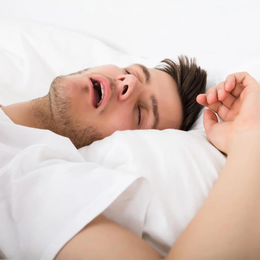 Man sleeping in a white bed with his mouth open