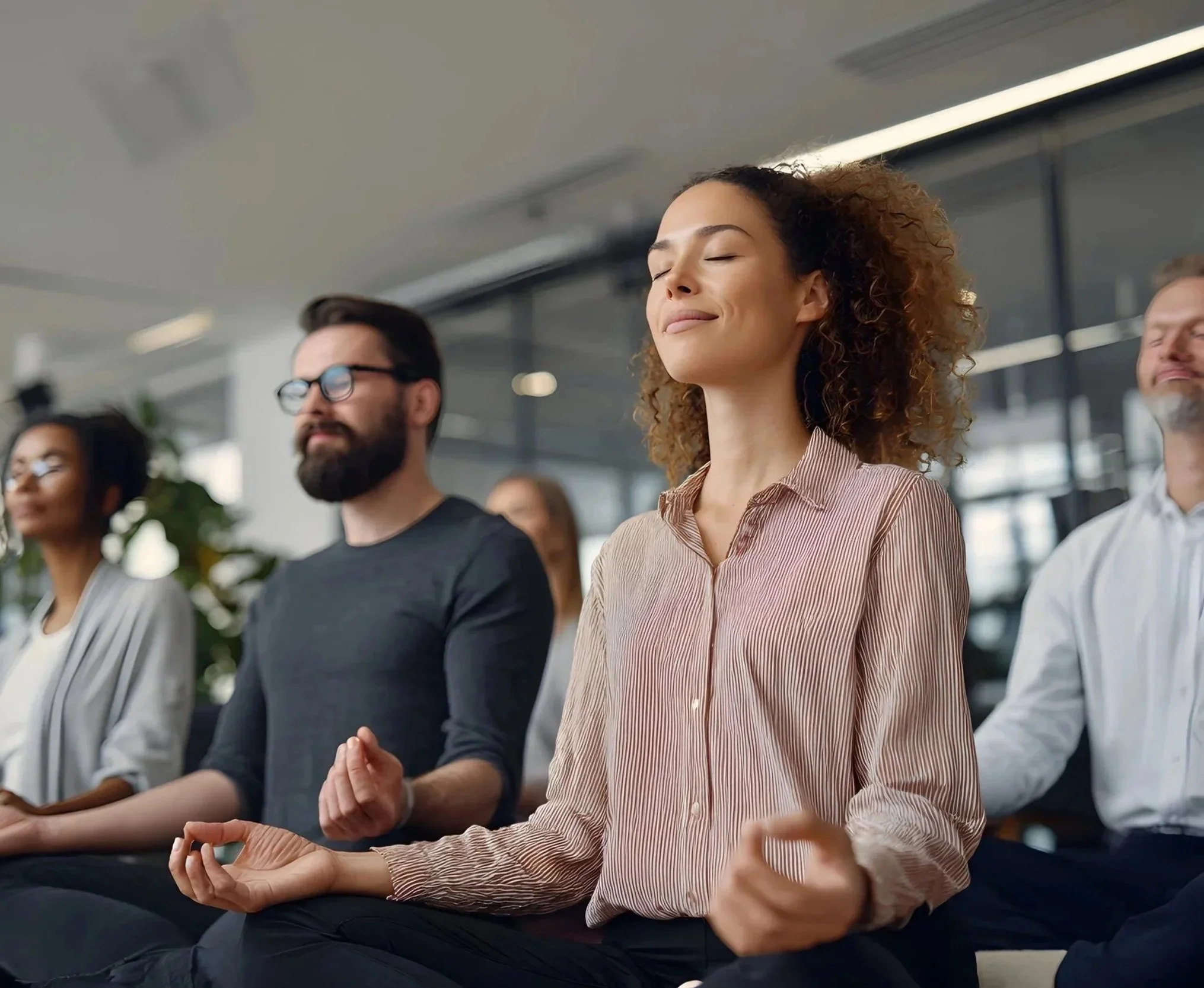 People sitting in meditation, eyes closed, practicing mindfulness or meditation in a modern office or conference room.