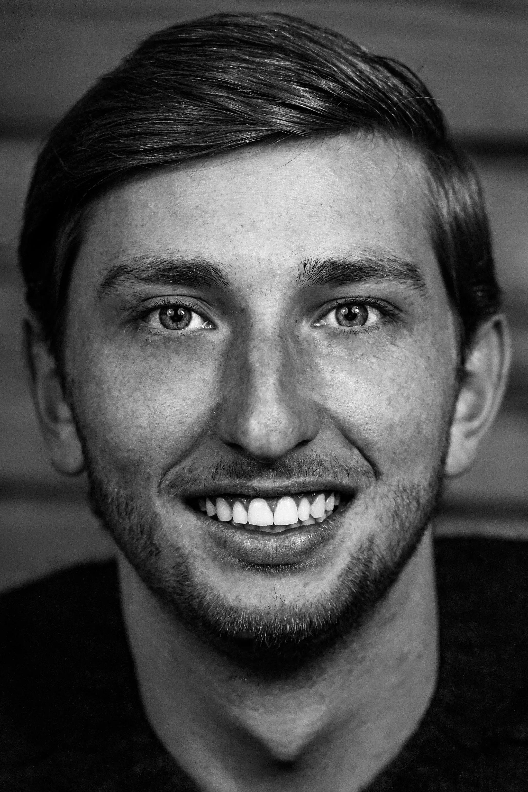 Portrait noir et blanc d'un jeune homme avec des cheveux courts, souriant, montrant ses dents, regardant directement l'objectif.