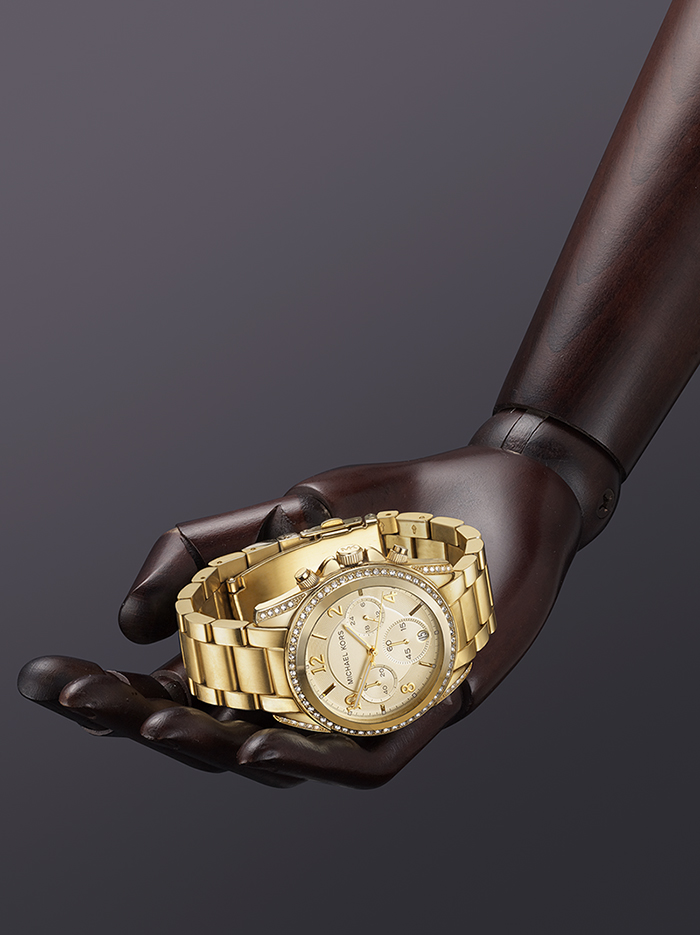 gold Micheal korrs watch places on mannequin hand against back background Creative watch photography