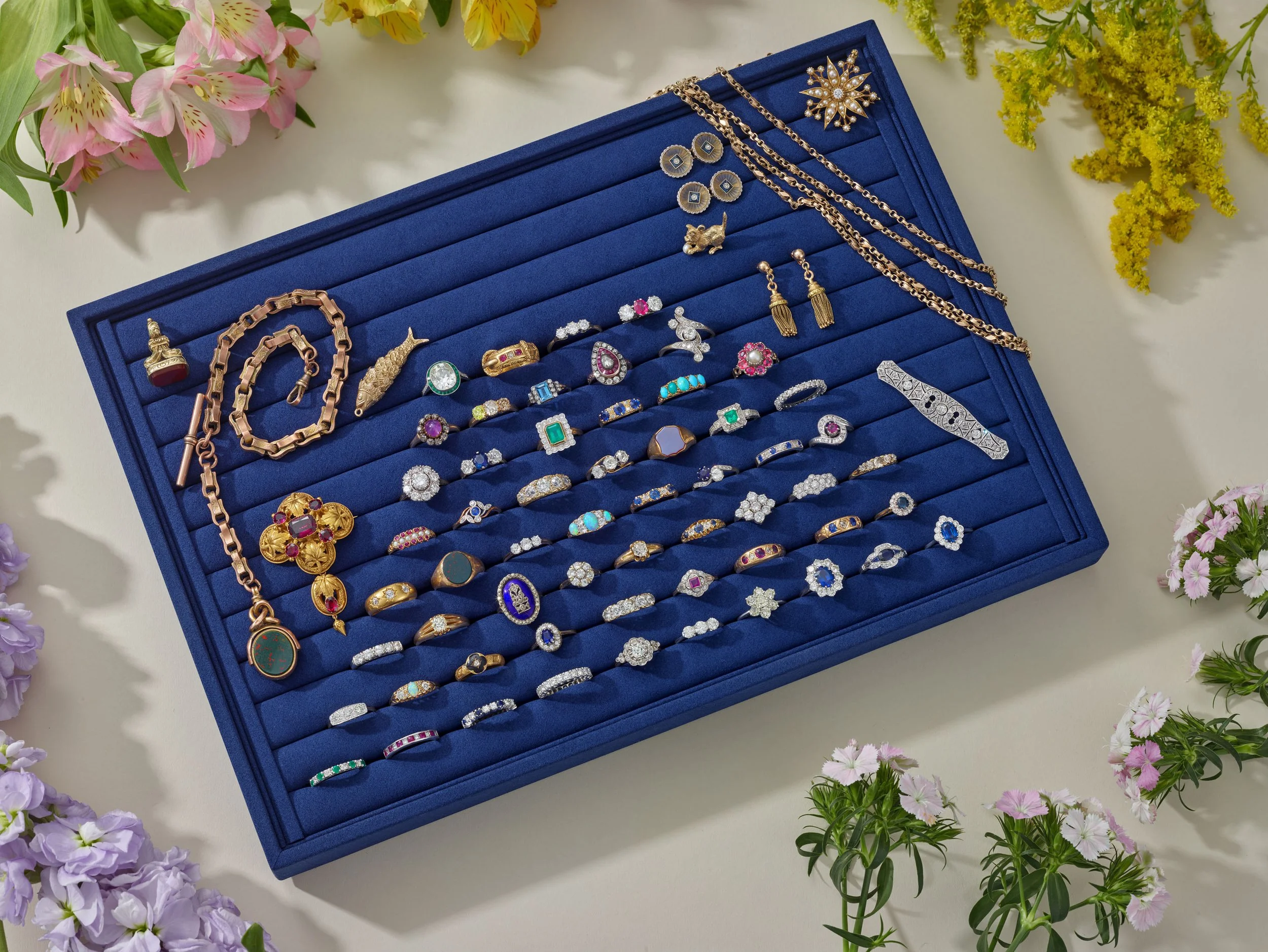 still life full collection of rings on blue velvet display surrounded by flowers creative jewellery photography 